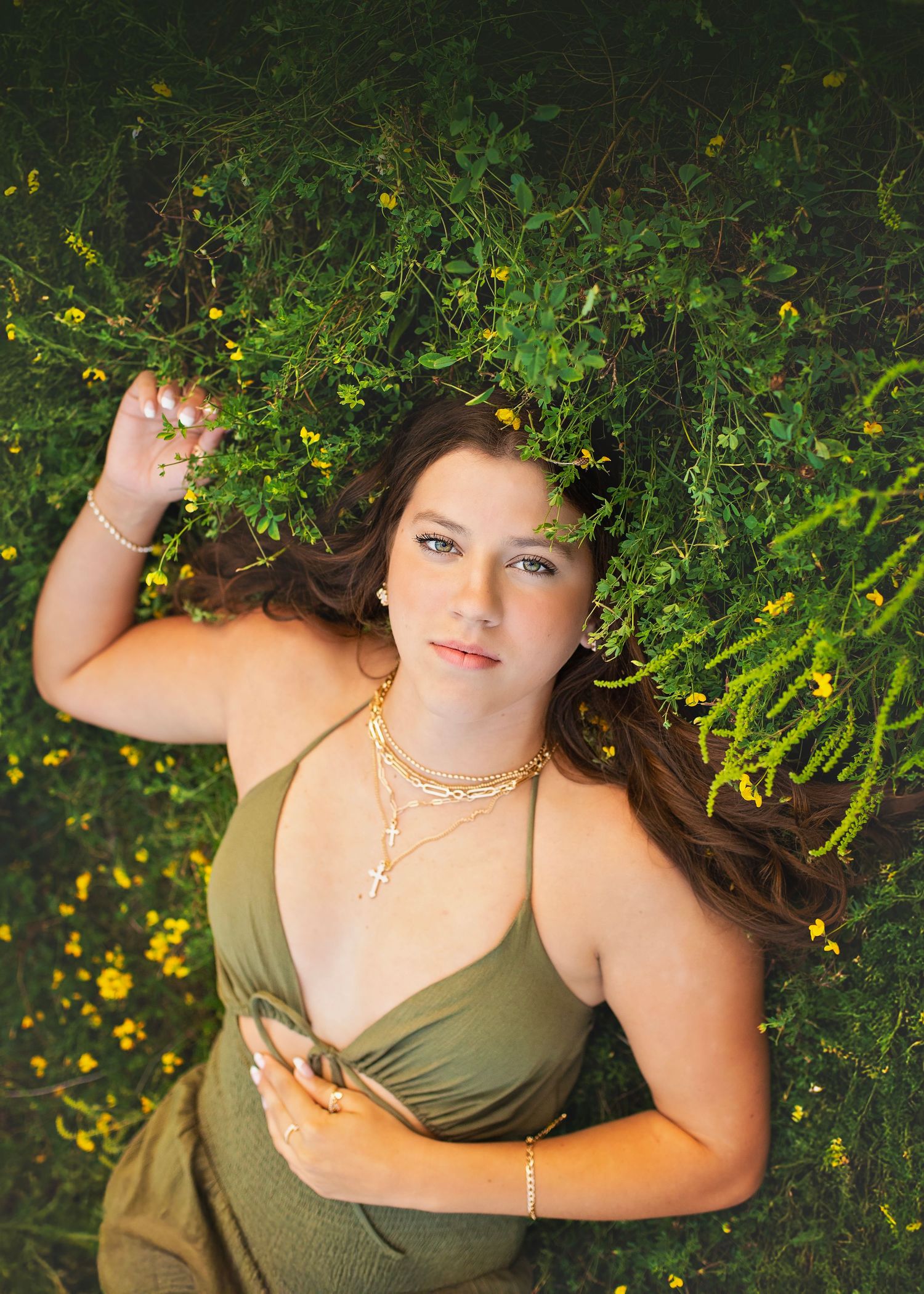 Young woman in olive dress lies among yellow wildflowers in lush green field.