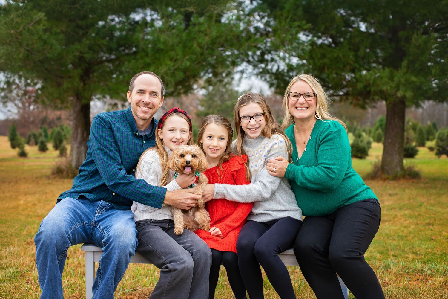 Happy family of five with golden dog posing at an outdoor Christmas tree farm.