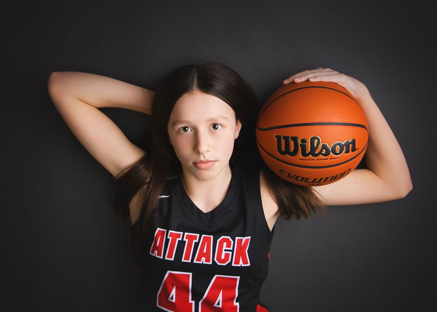 Young basketball player in Attack jersey number 44 poses with Wilson ball overhead.