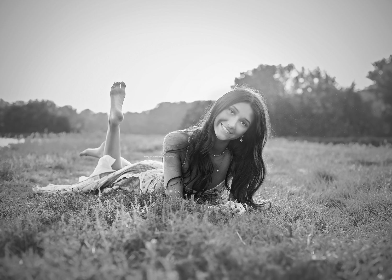 Black and white photo of a young woman with long hair lying in a grassy field, looking back at the camera.