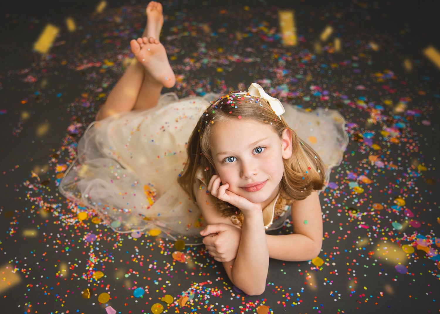 Blonde girl in white tulle dress lying on confetti-covered studio floor.