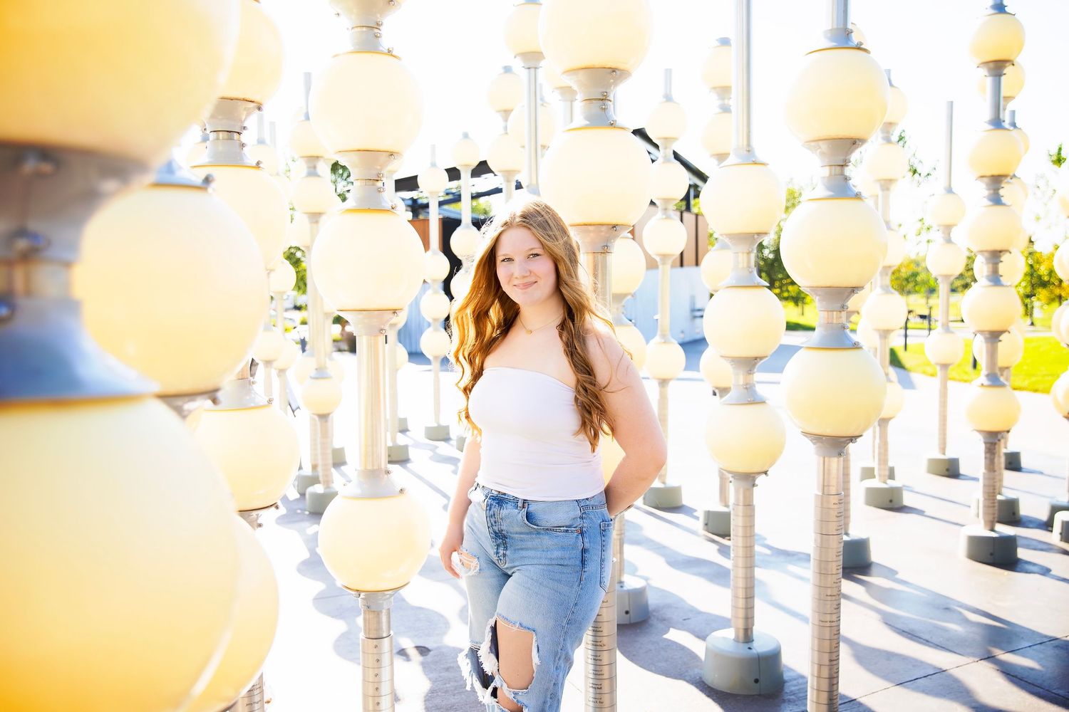 Teen girl in white top and ripped jeans poses among yellow globe light installations.