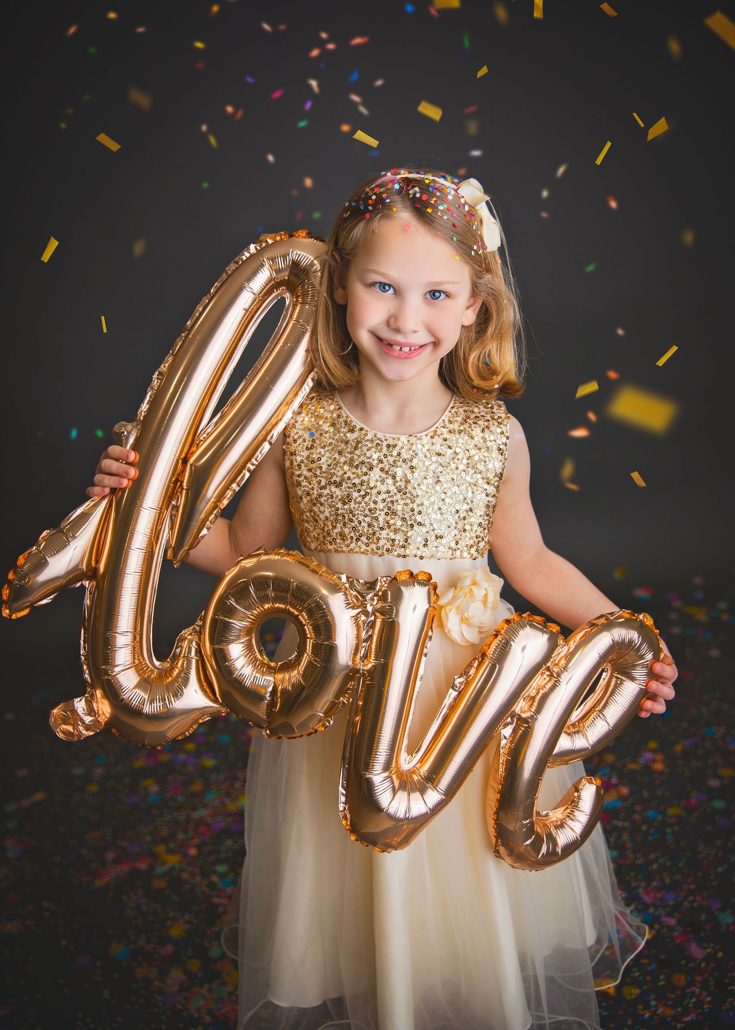Smiling girl in gold sequin dress holding a gold love balloon.