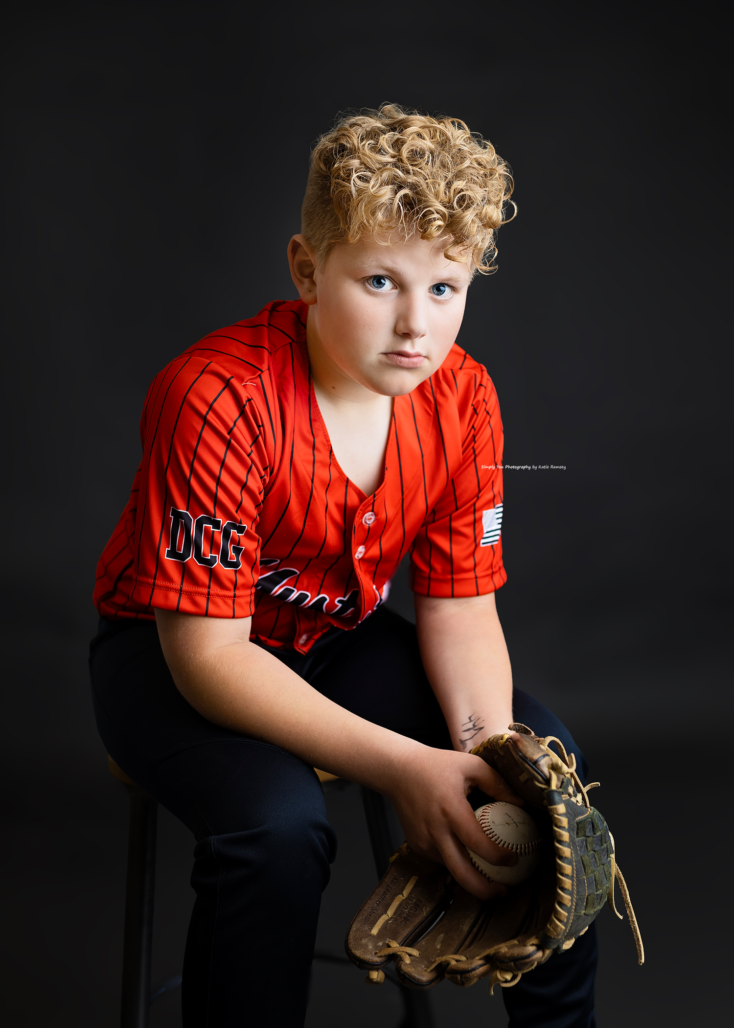 Young baseball player in red jersey holding glove, posed for team portrait.