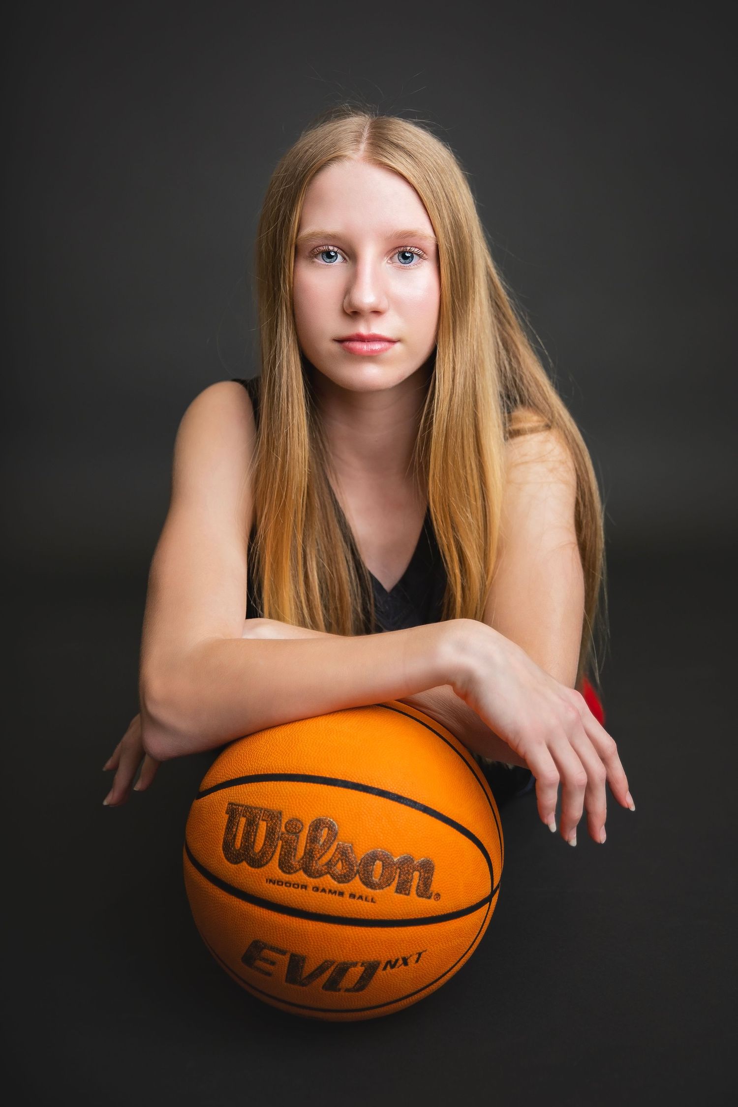 Teen girl leaning on Wilson EVO NXT basketball in black jersey.