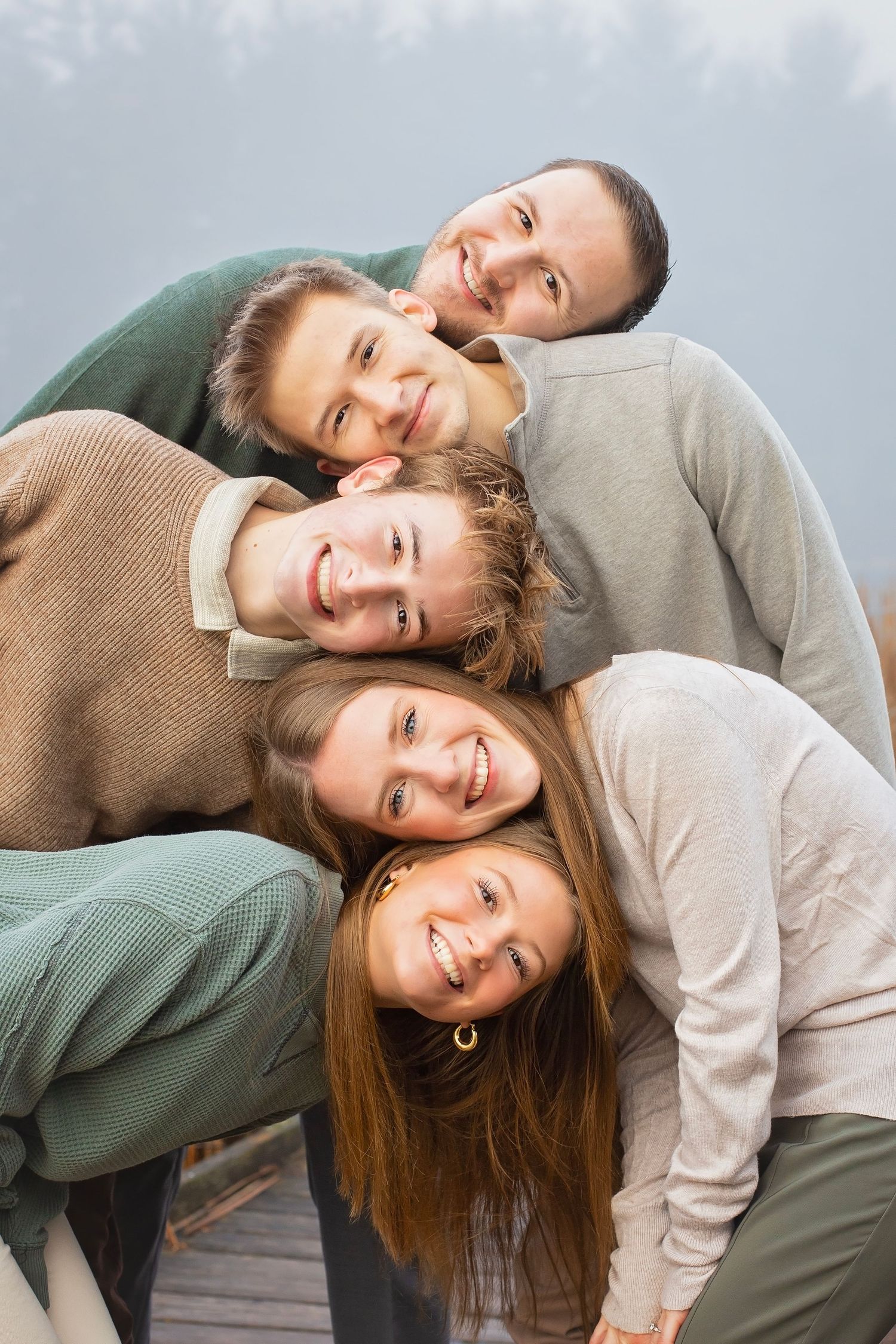 Five smiling people stacking their heads together in a playful pyramid pose outdoors.
