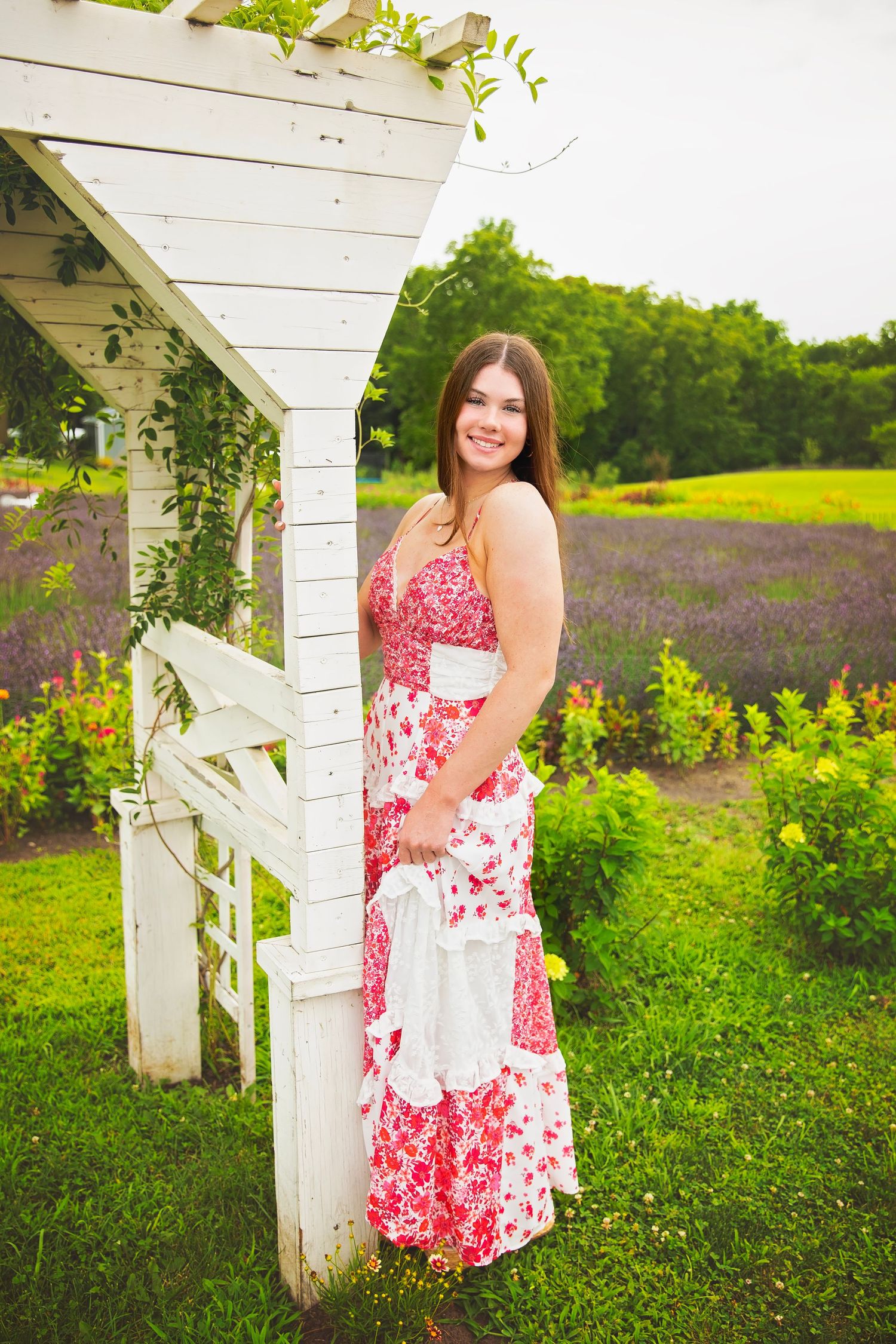 Young woman in red floral maxi dress standing by white arbor.