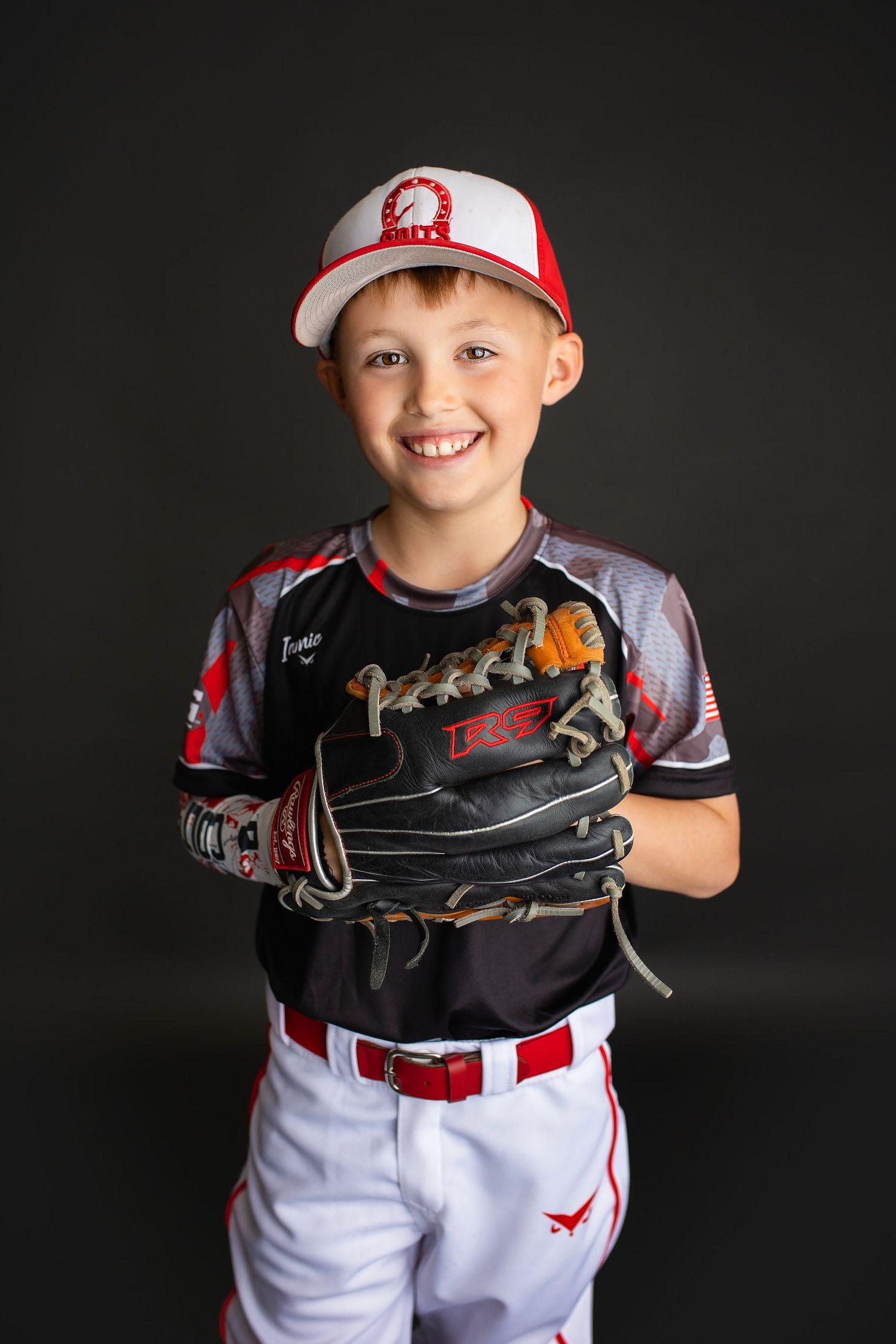 Smiling young boy in Colts baseball uniform holding glove on dark studio background.