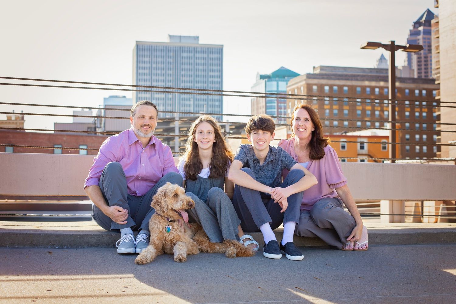 Family of four with a golden doodle sitting on a rooftop with city skyline.