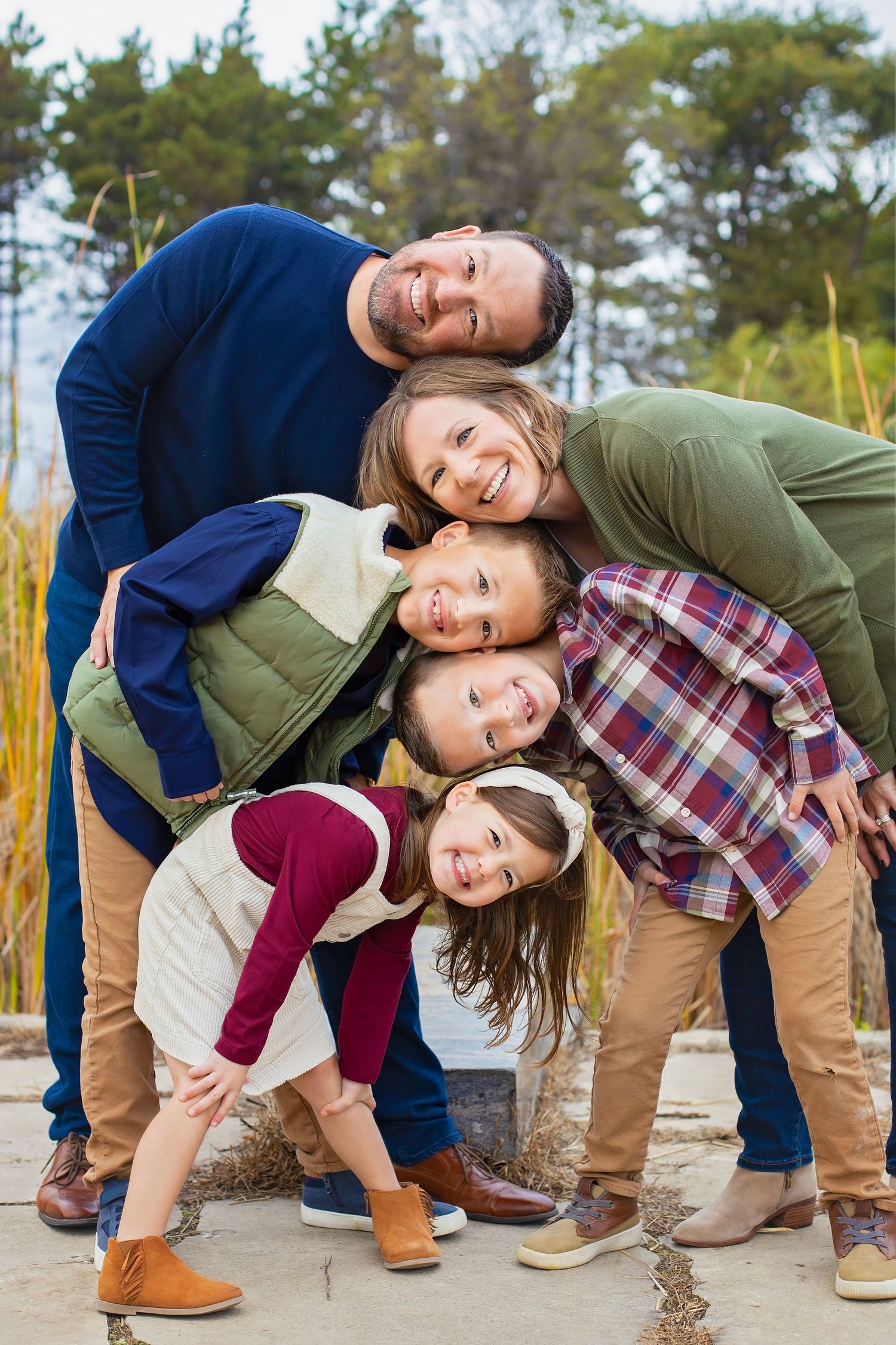 A joyful family of five stacks their heads together for a fun outdoor portrait surrounded by autumn foliage.