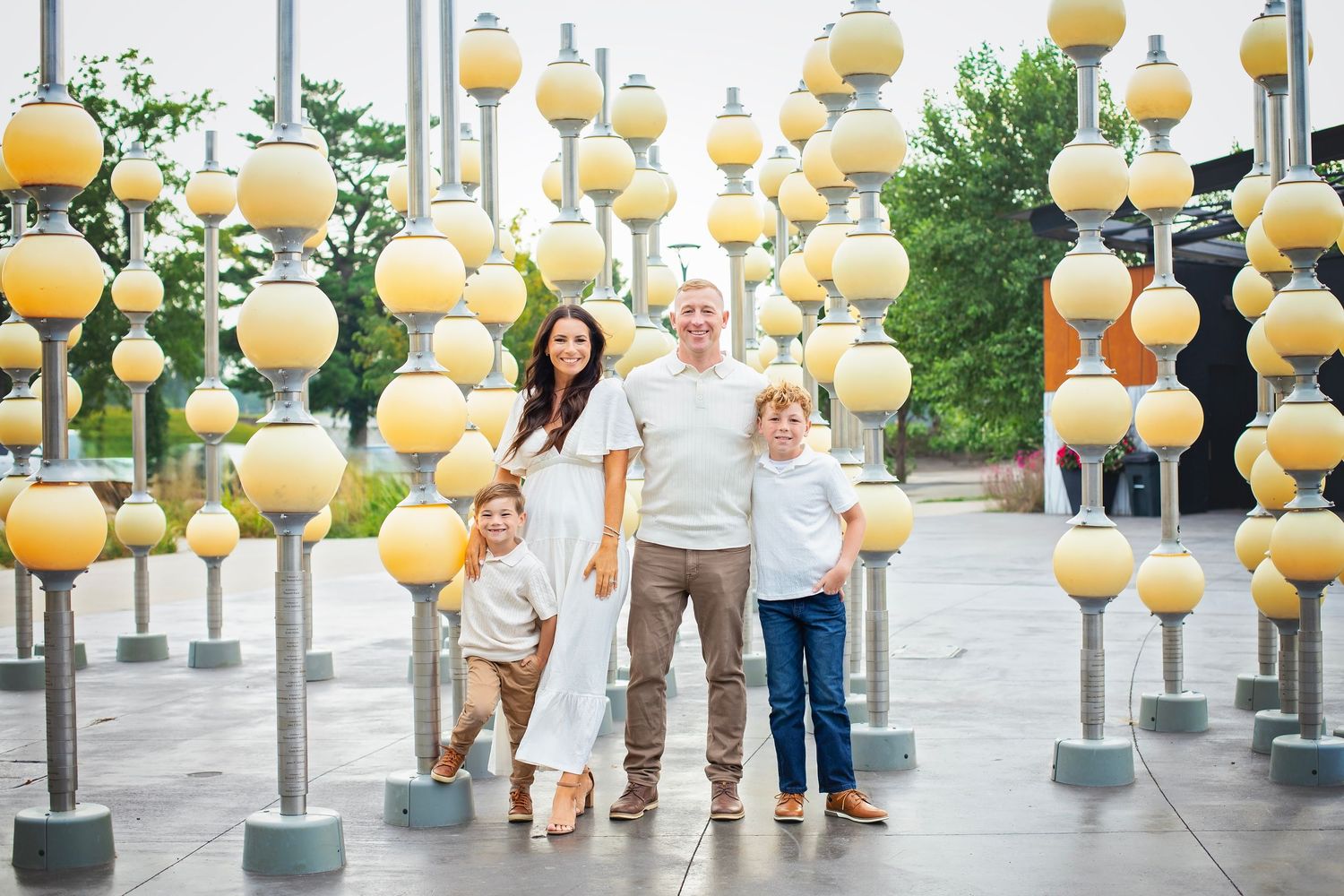 Family of four posing among decorative yellow globe light sculptures at an outdoor urban plaza.