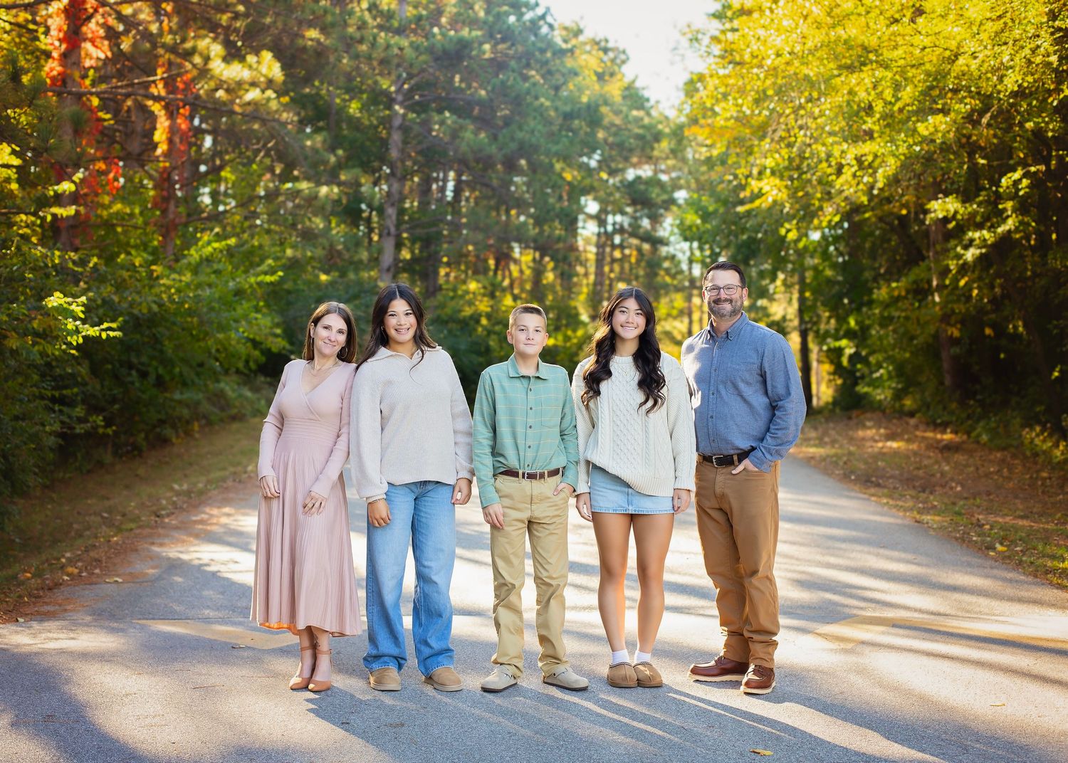 Family of five smiling on a tree-lined road during golden autumn afternoon.