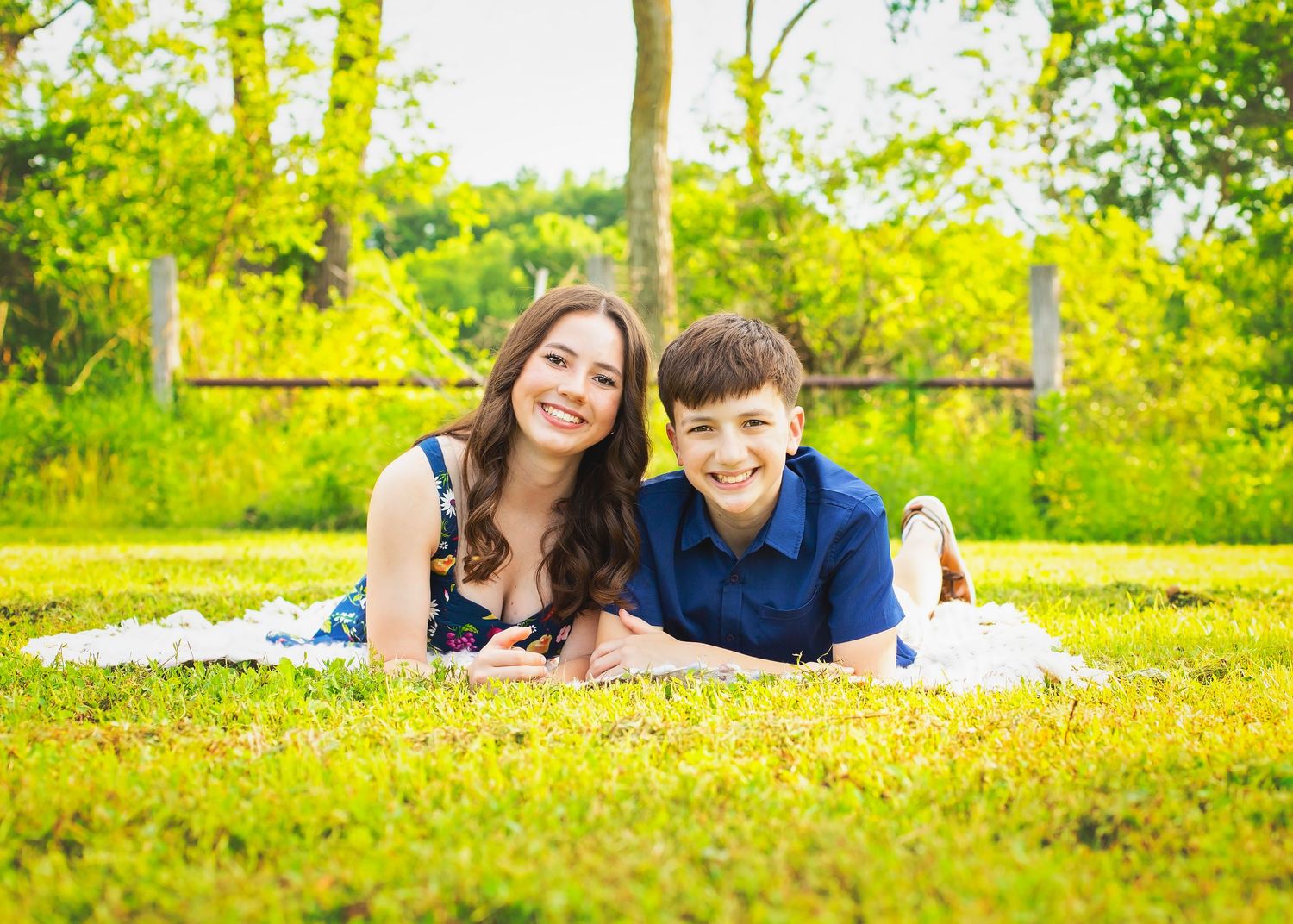 Two siblings lying on grass smiling during sunny outdoor family photo session in green park.