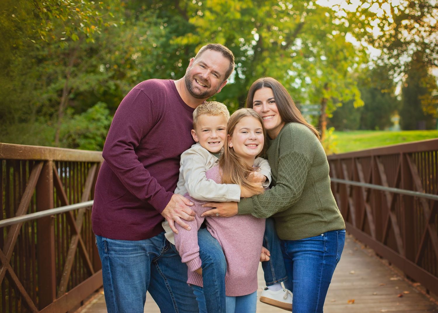 A loving family of four shares a warm hug on a wooden bridge outdoors.