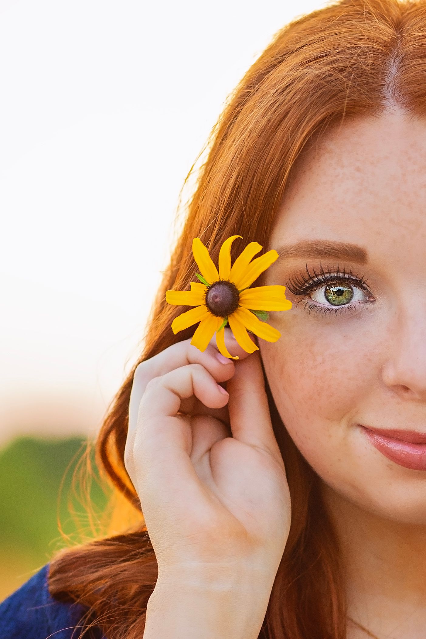 Close-up of freckled redhead girl with green eyes holding yellow black-eyed Susan flower beside her face.