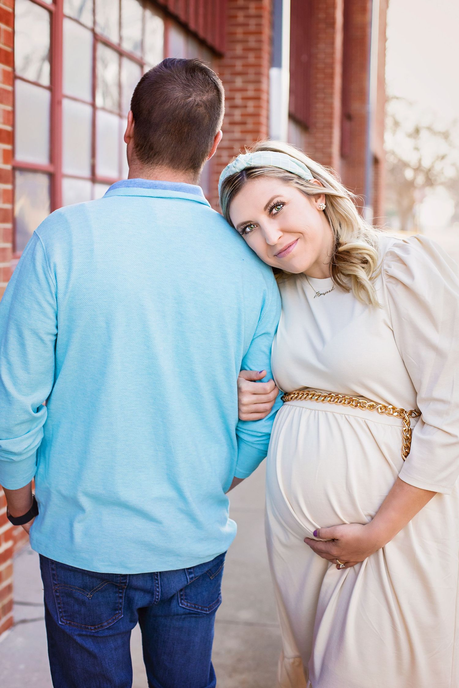 Pregnant woman in white dress leans on partner's shoulder during maternity shoot.