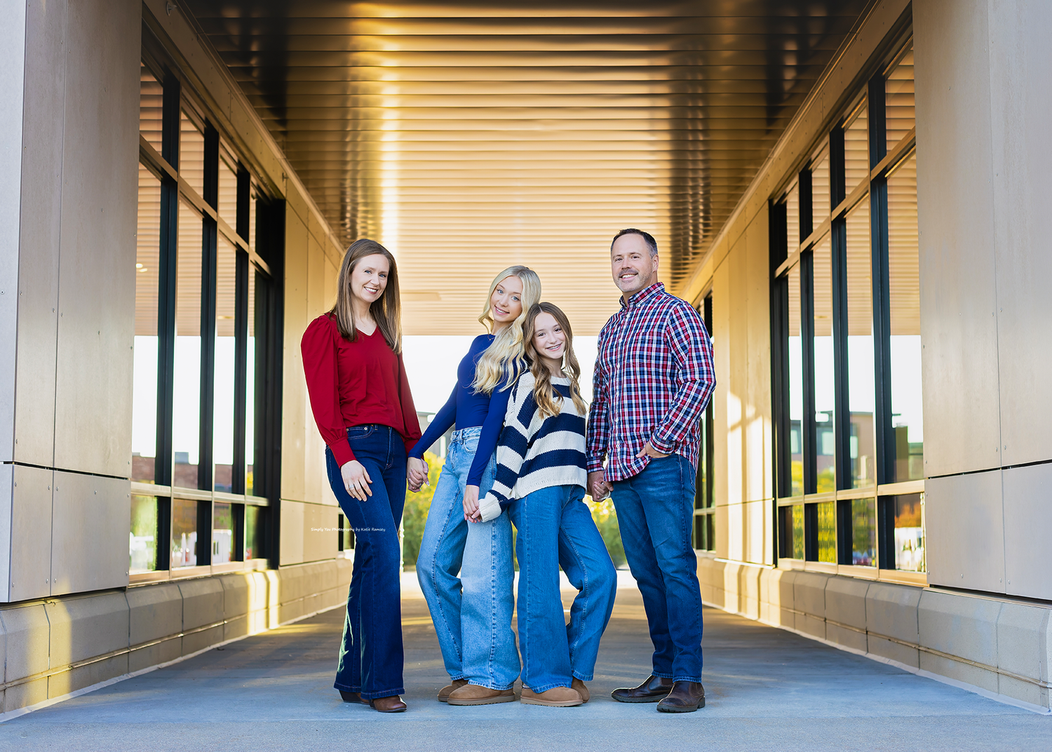 Family of four posing together on a modern walkway, wearing coordinated red, navy, and plaid outfits for a portrait.