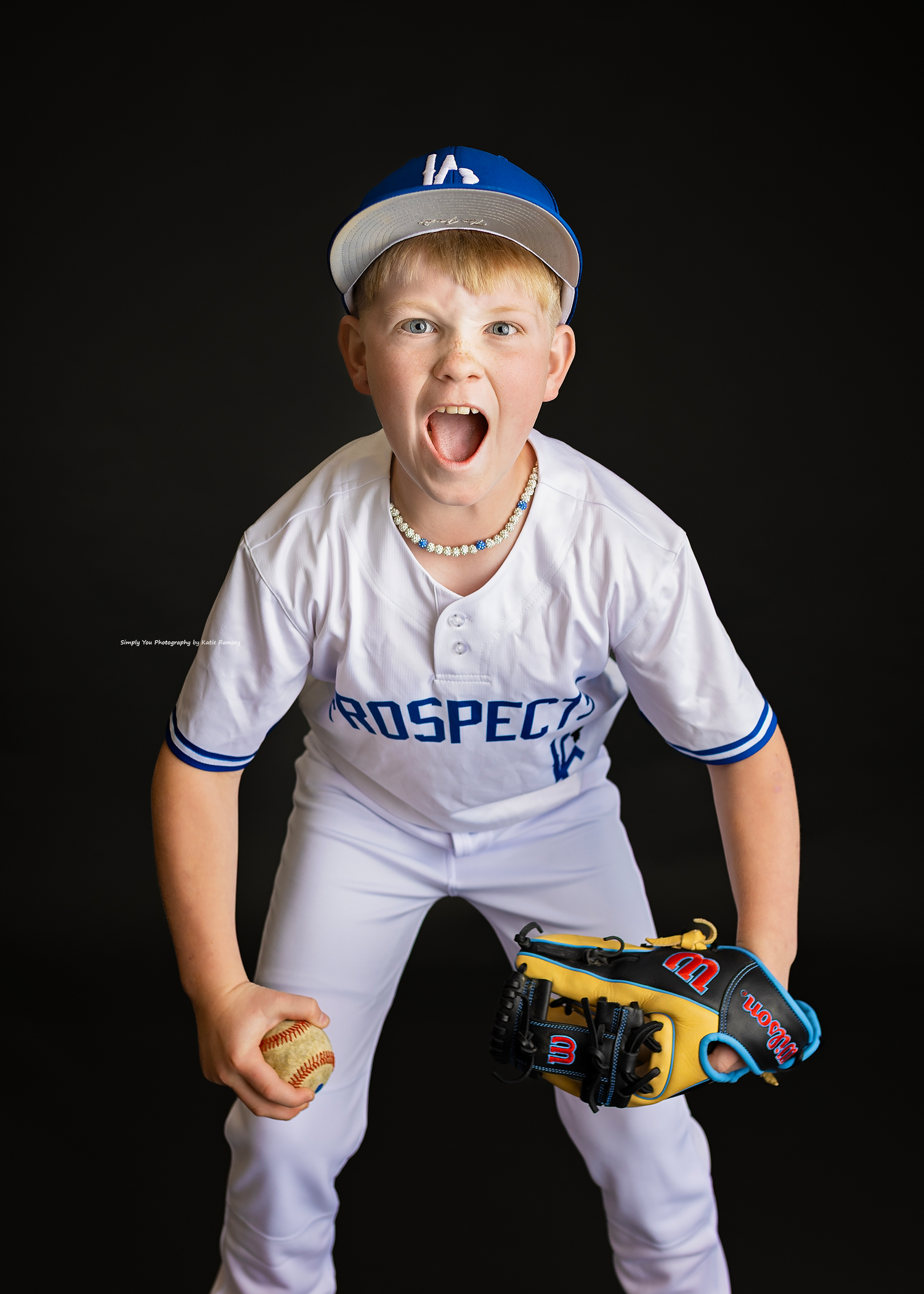Energetic boy in Prospects baseball uniform screaming with glove and ball on black background.