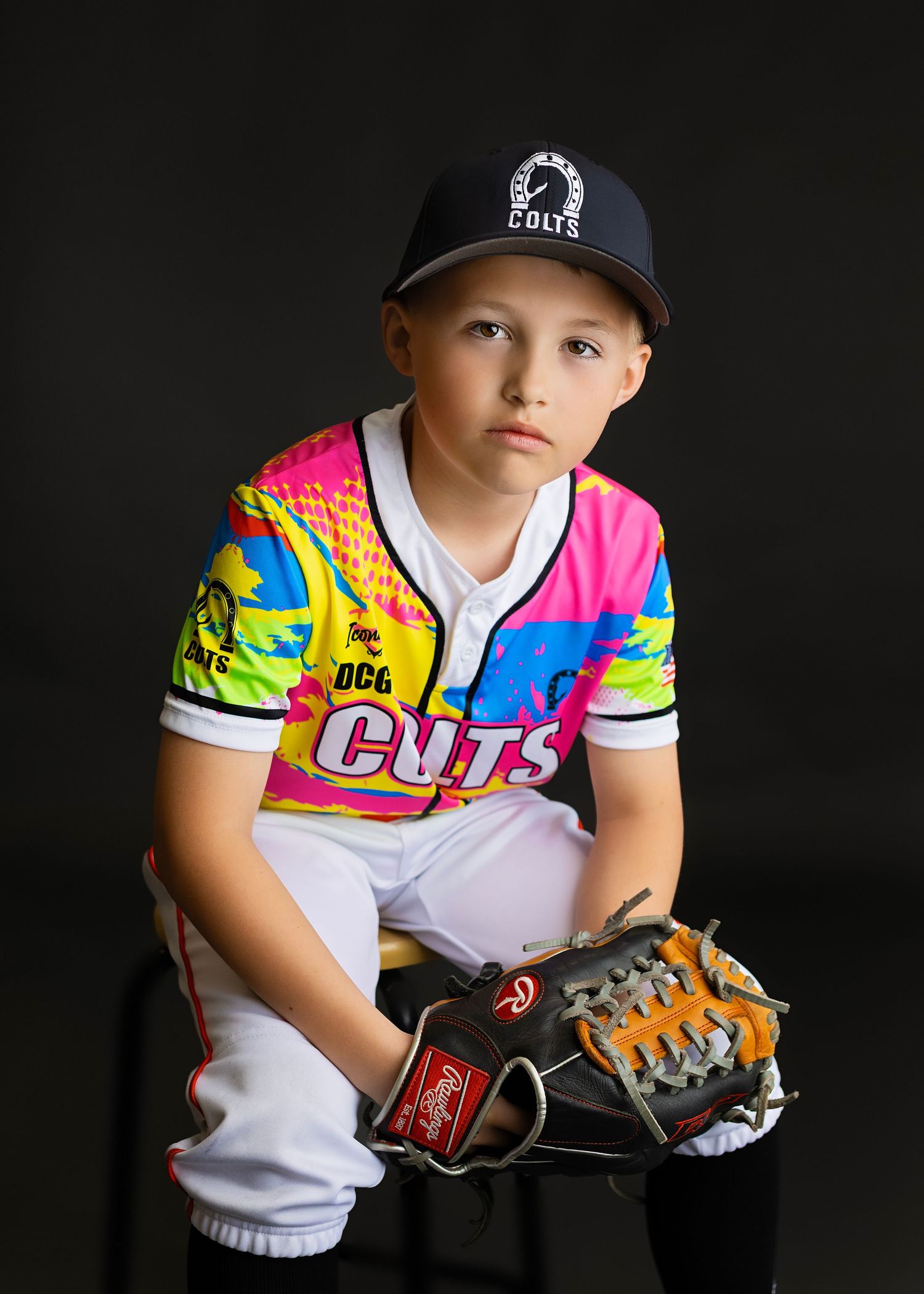 Young baseball player in colorful Colts jersey and cap poses with Rawlings glove for team portrait.