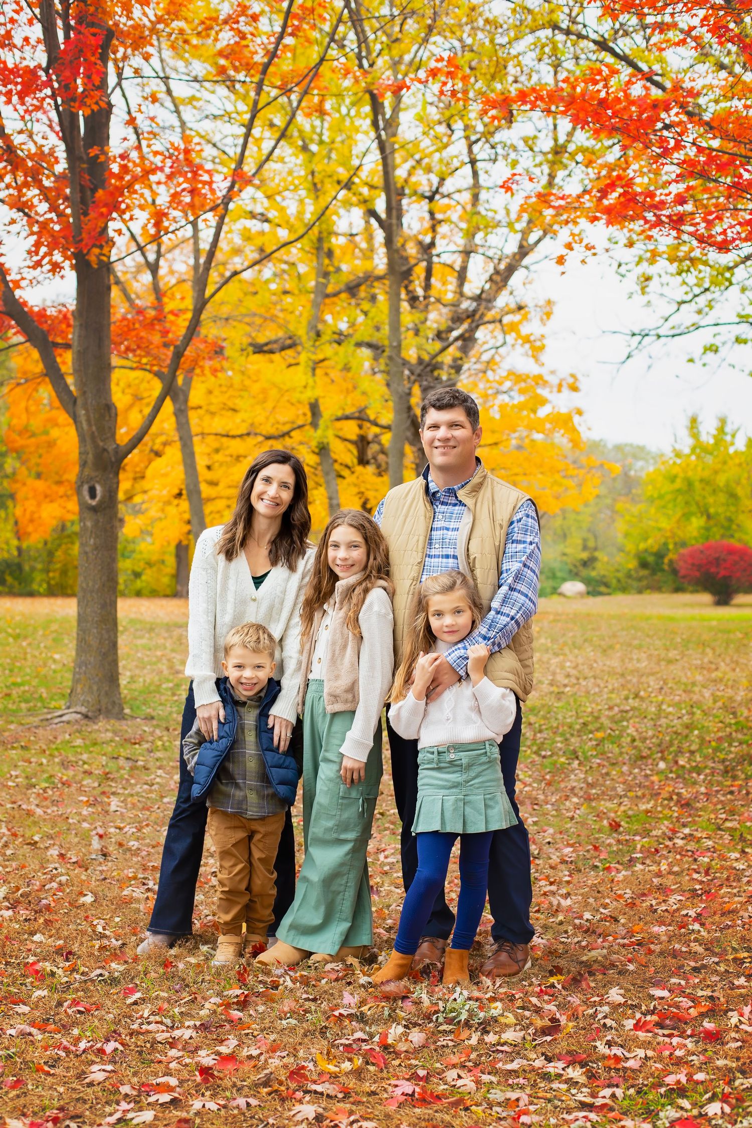 Family of five standing together in a park with vibrant red and orange fall foliage.