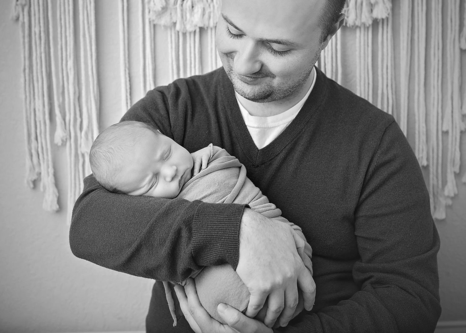 Black and white portrait of father tenderly cradling sleeping newborn baby in his arms.