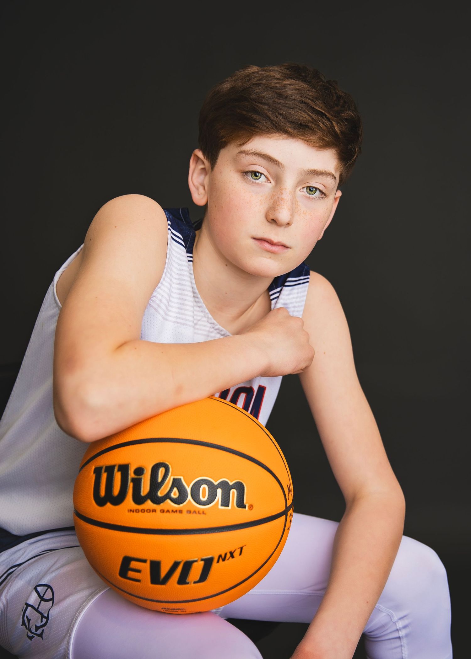 Young male basketball player posing with Wilson EVO NXT ball in white jersey.