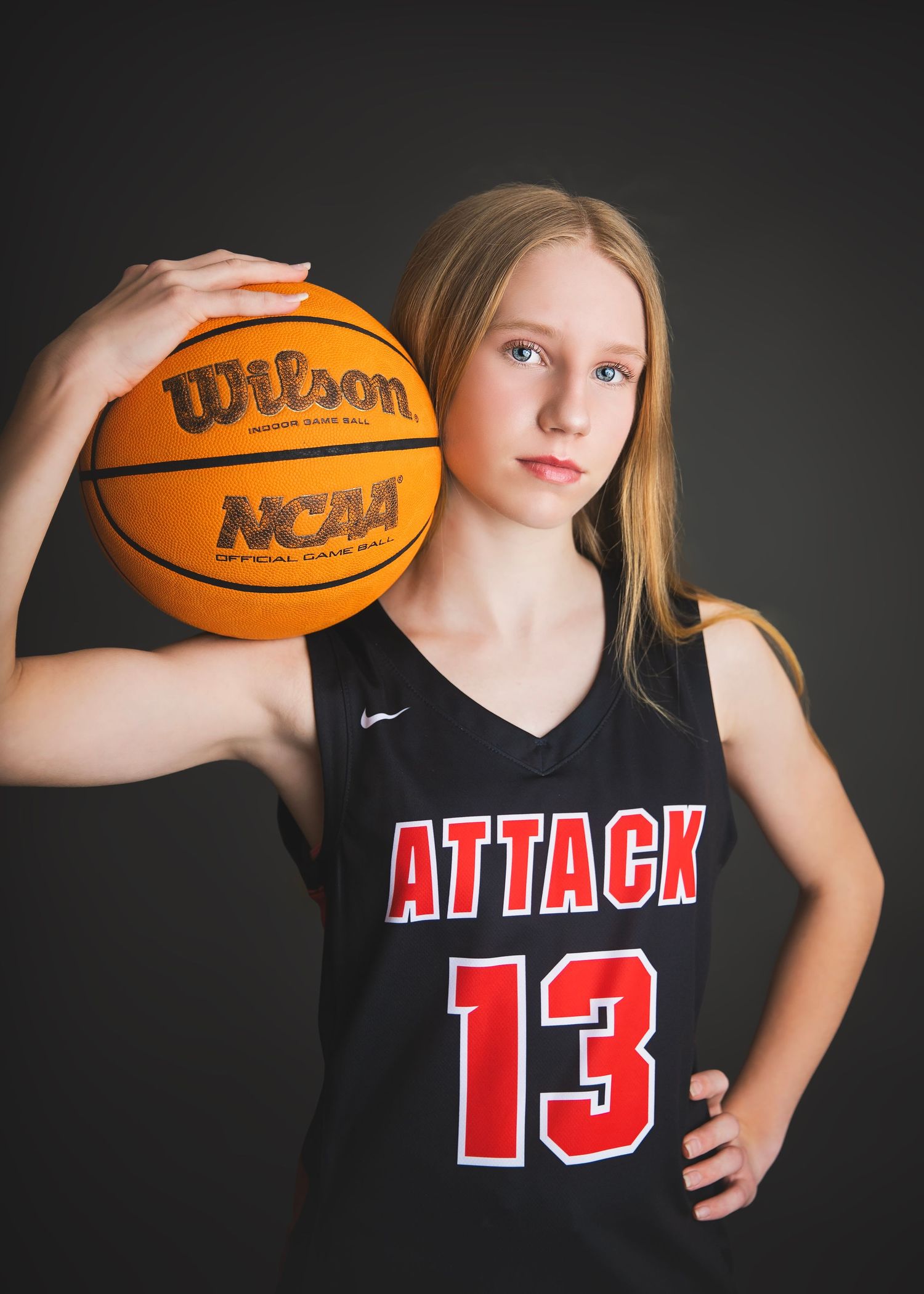Young female player in Attack 13 jersey holding Wilson NCAA basketball.