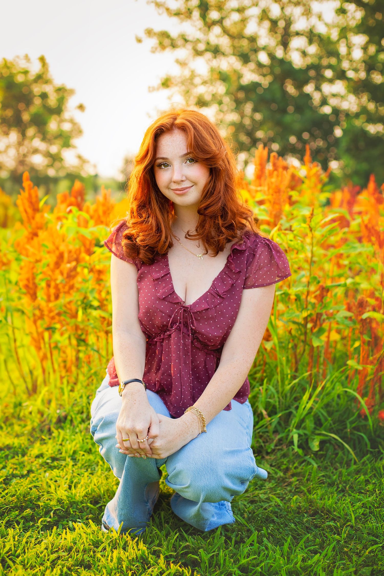 Young redhead woman crouching in a vibrant garden with orange flowers during golden hour.