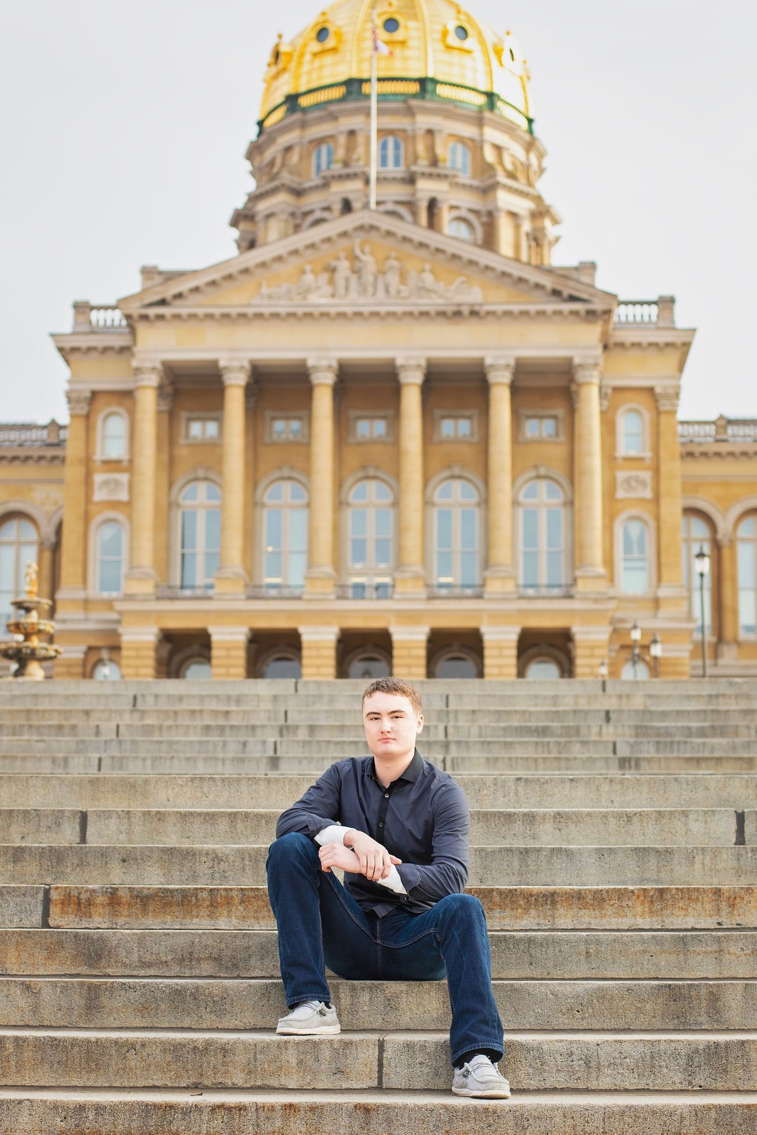 Young man sitting on steps of a grand capitol building with golden dome.