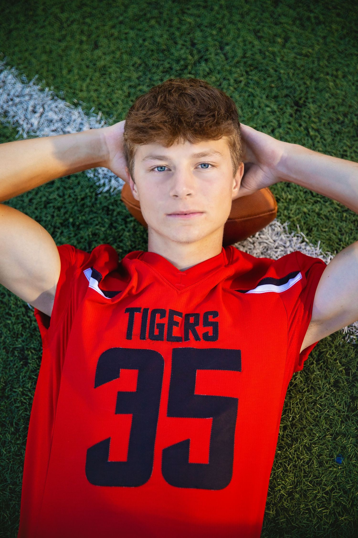 Teen football player in red Tigers jersey number 35 lying on a grass field looking up.