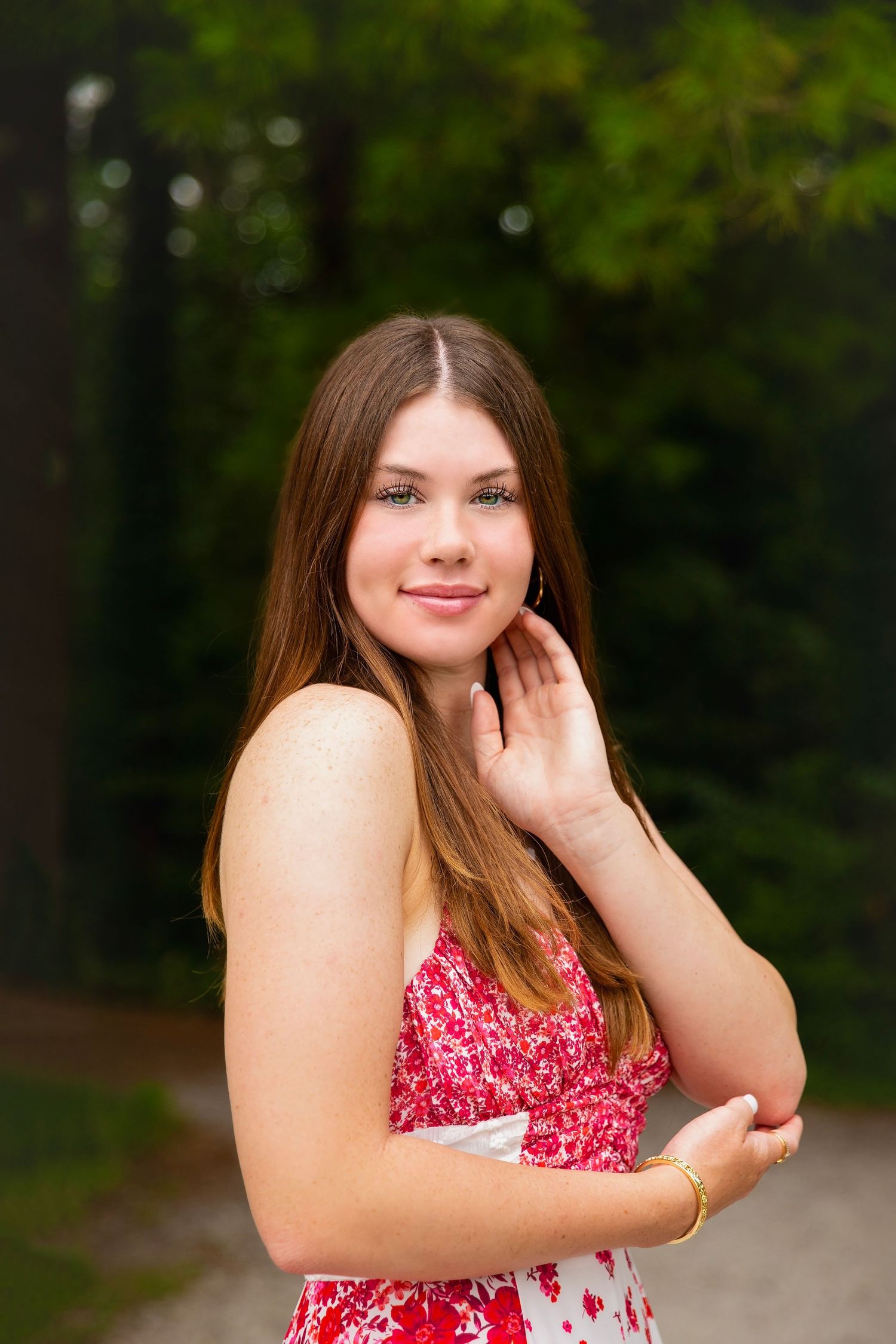 Pretty teen girl in red floral dress posing outdoors in forest.