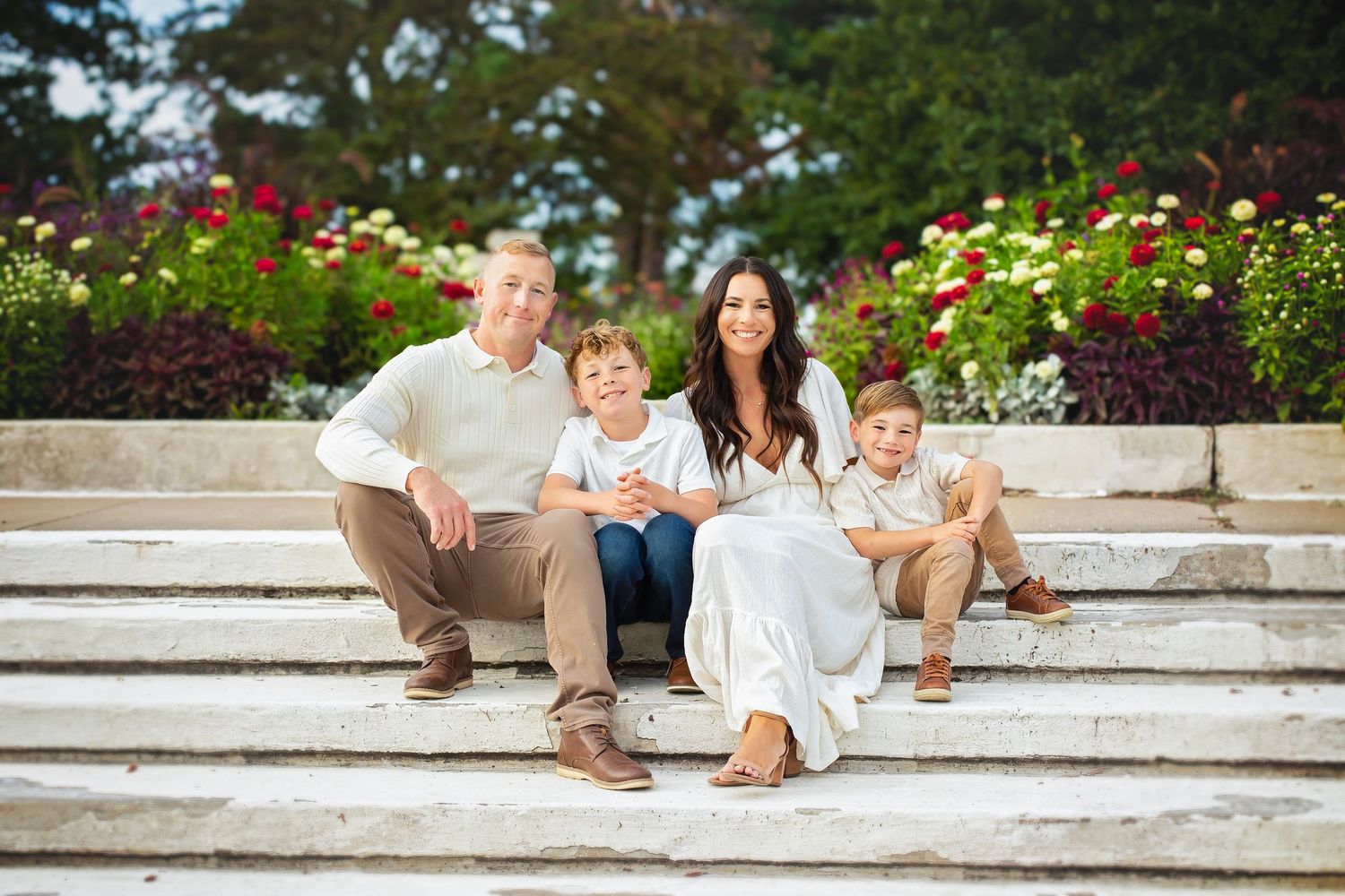 Family of four sitting on wide stone steps with vibrant flower garden in the background.