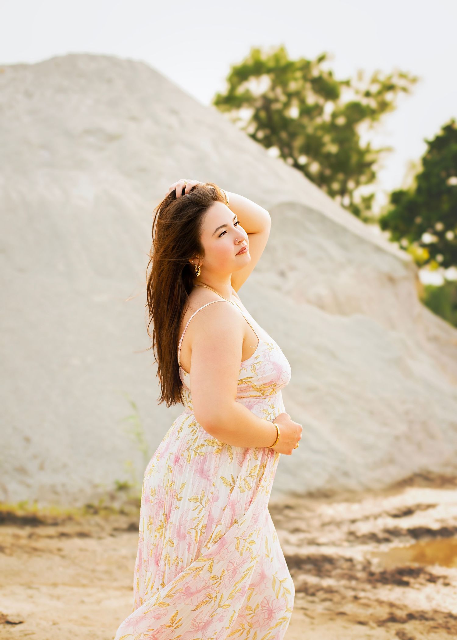 Young woman in floral sundress poses in front of a large white rock formation outdoors.