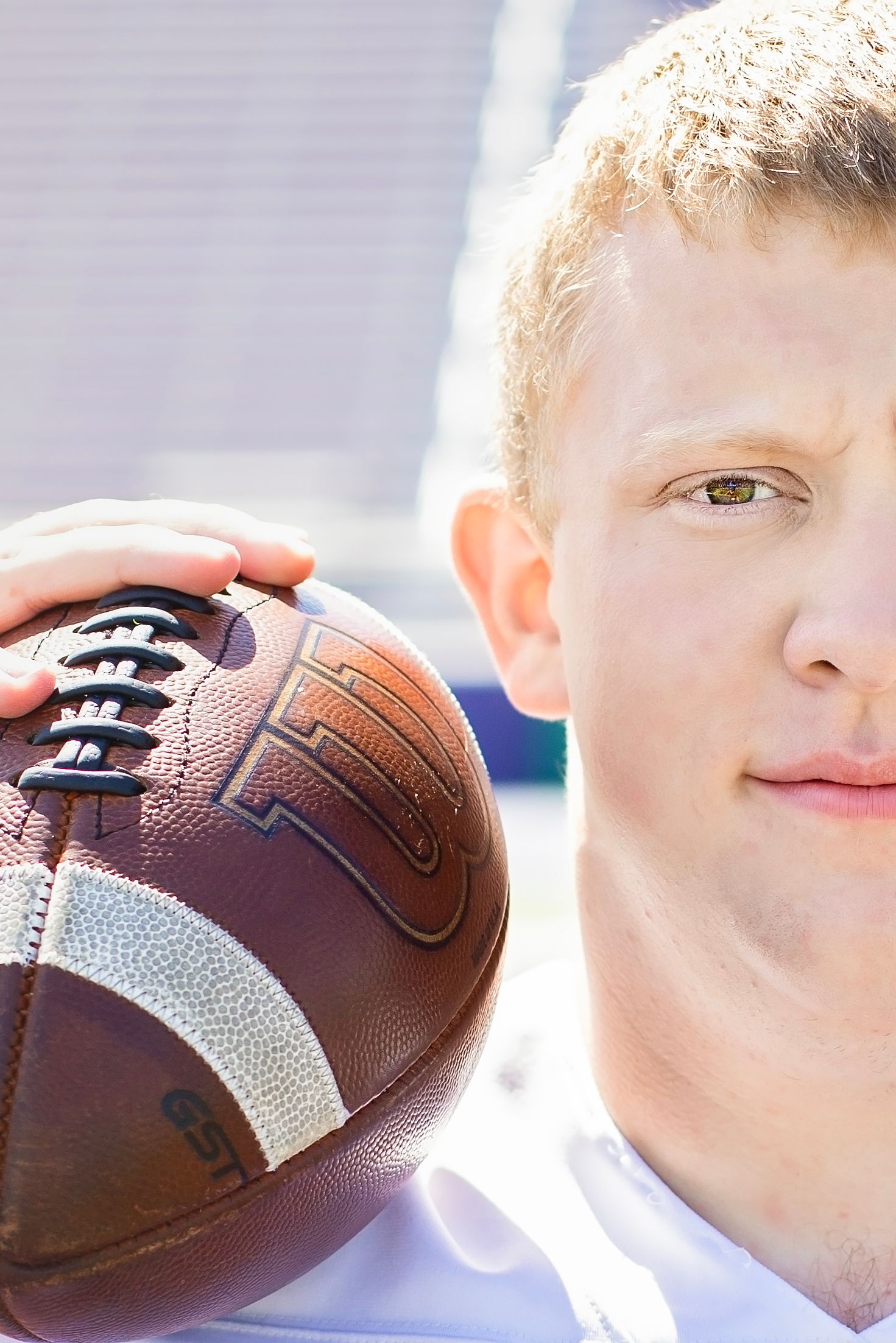 Close-up of young male football player holding a Wilson football beside his face outdoors.