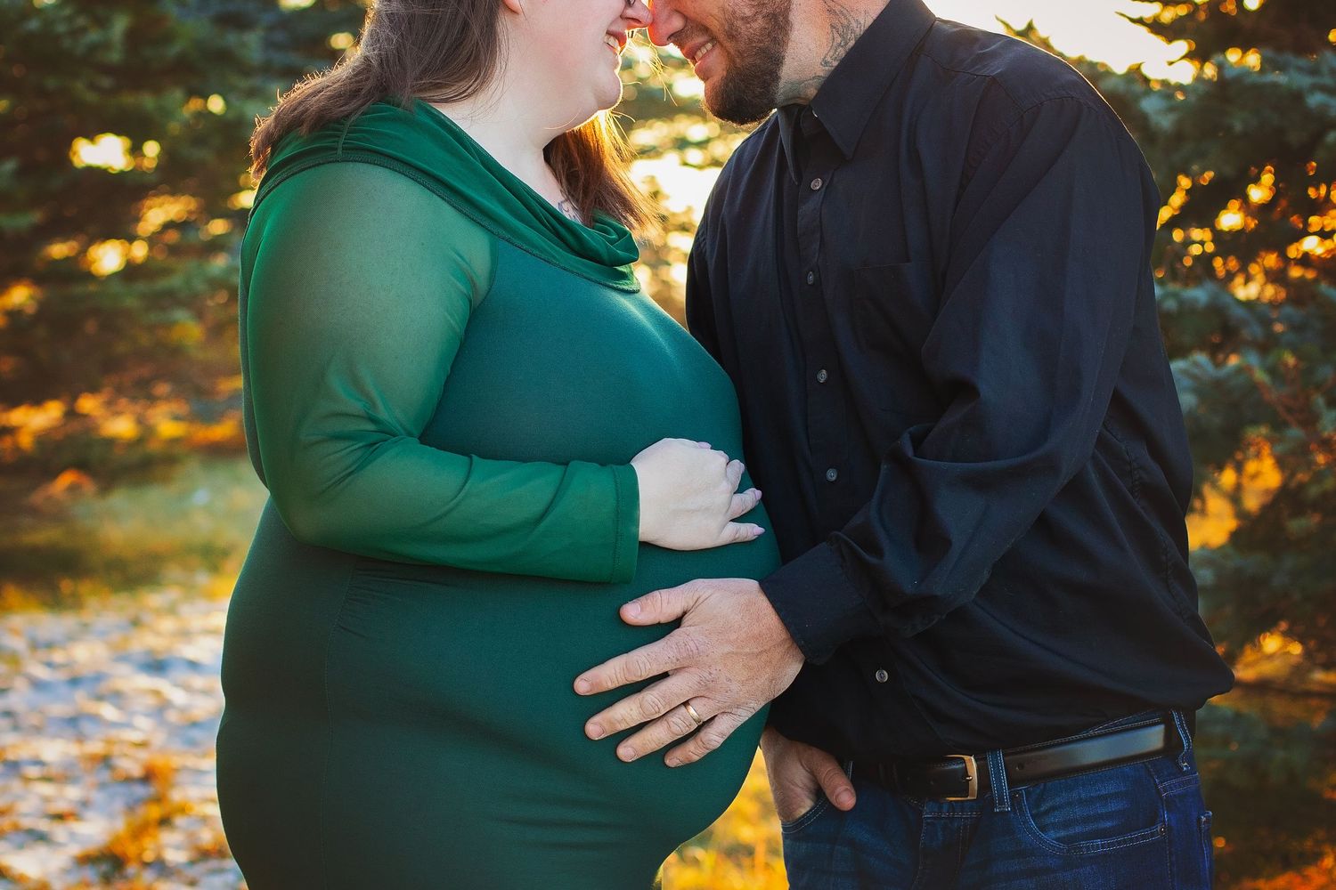 Close-up of pregnant woman in green dress and partner holding baby bump outdoors.