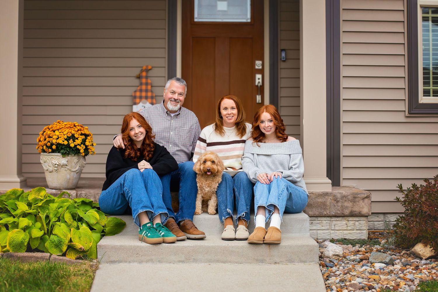 Family of four with a golden doodle dog sitting on front porch steps in autumn.