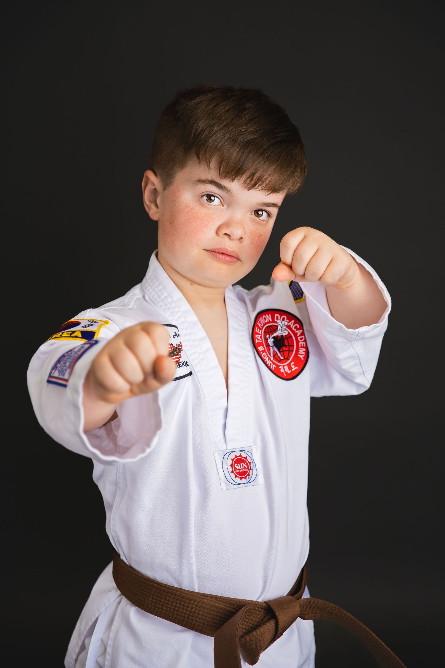 Young martial artist in white gi with brown belt strikes fighting pose in studio photo.