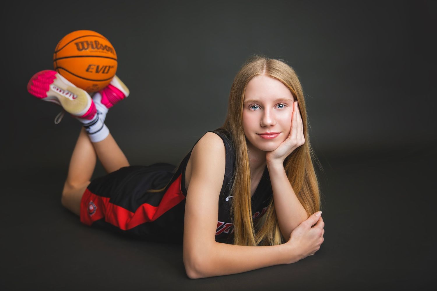 Young girl in Attack basketball uniform lying down with Wilson ball.