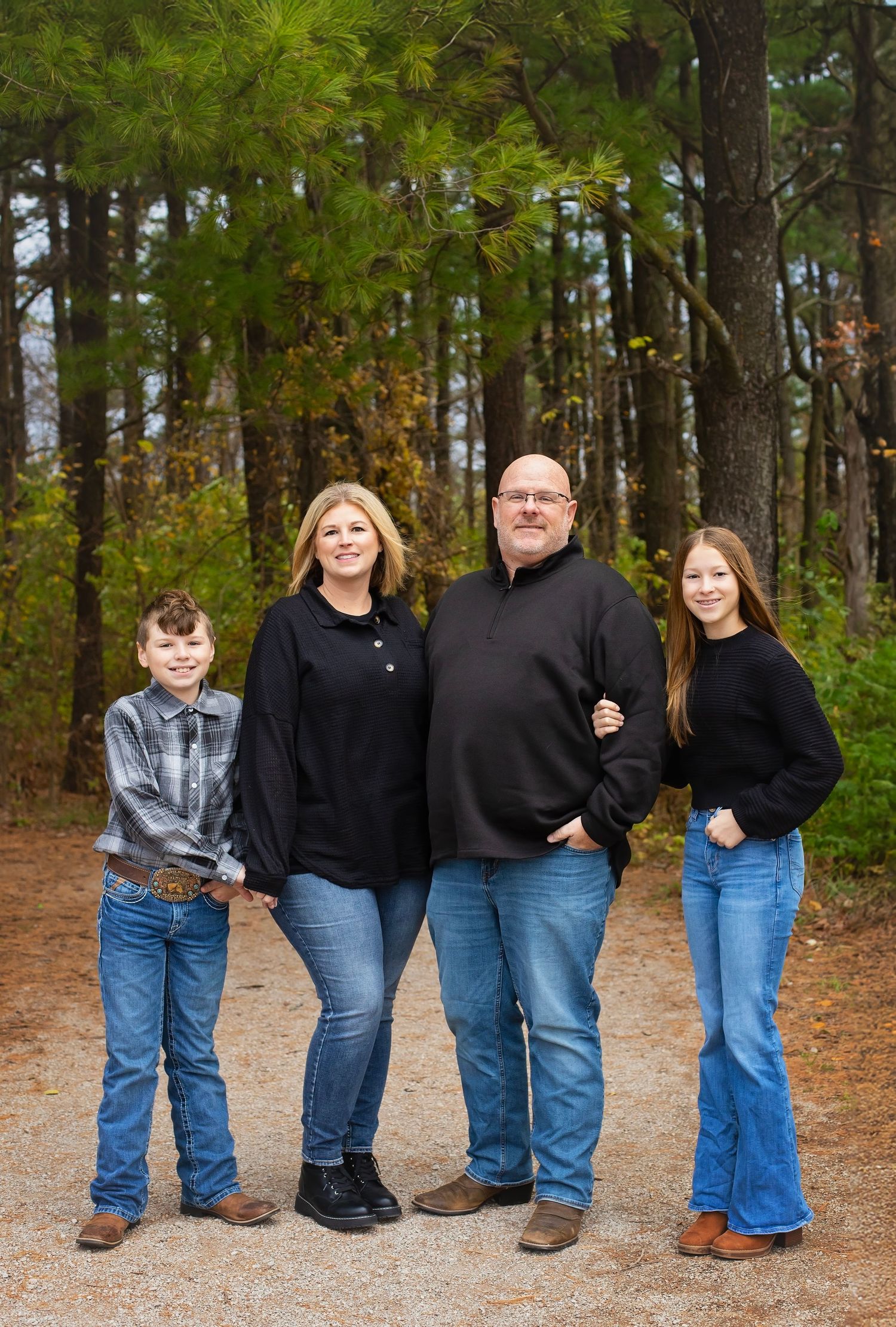Family of four posing on a forest path in matching black outfits.