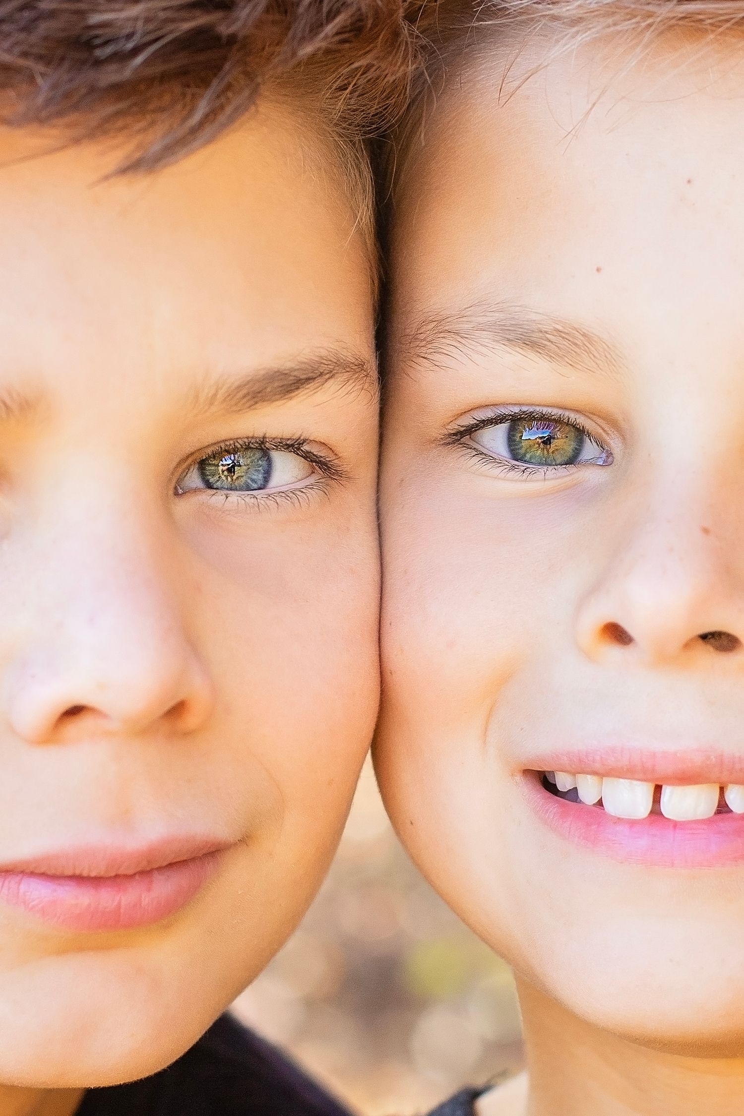 A close-up portrait of two children pressing their heads together, both with striking green eyes and bright smiles.