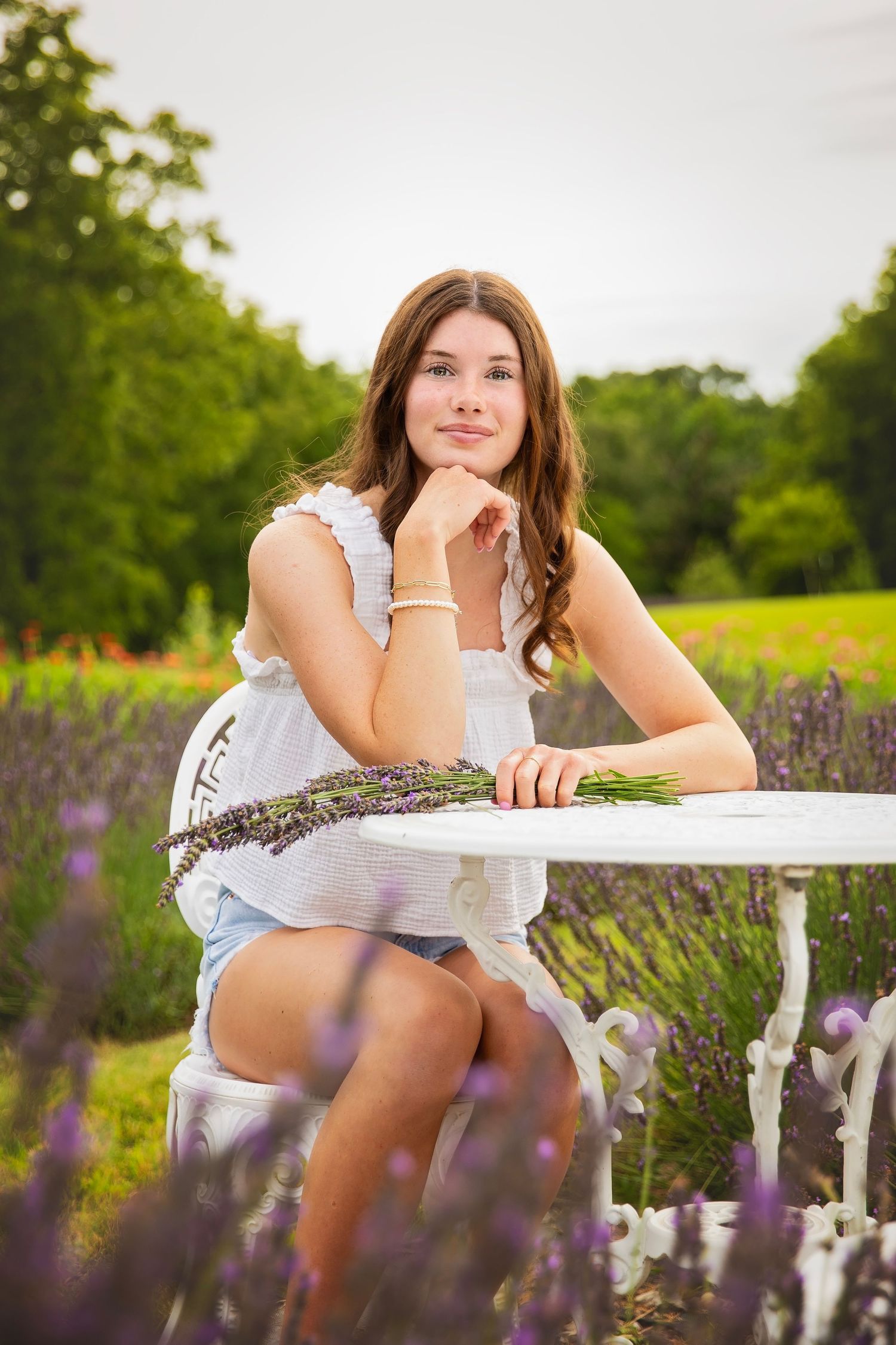 Teen girl sitting at white table in lavender field holding fresh lavender bouquet.
