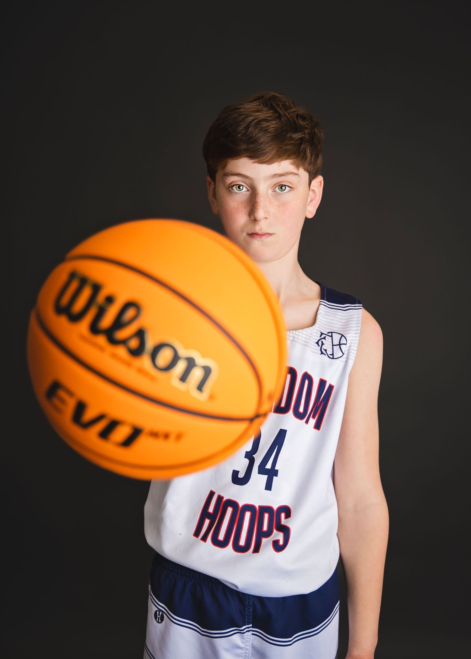 Young boy in Kingdom Hoops number 34 jersey extending a Wilson basketball toward the camera.
