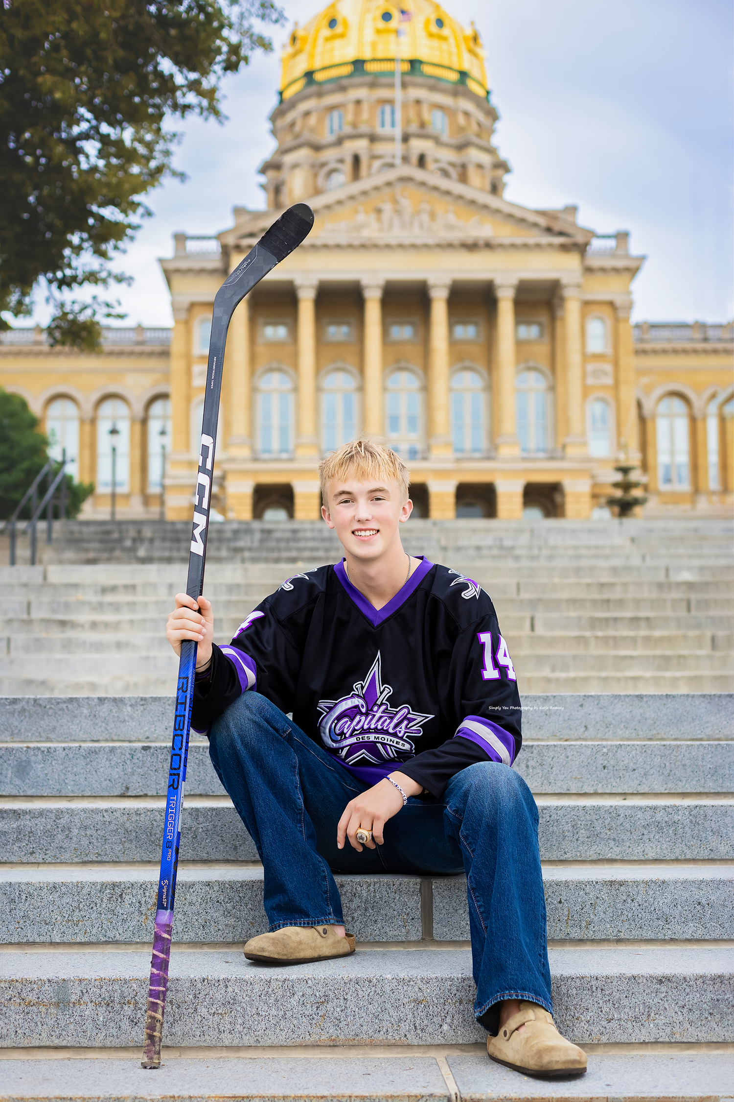 Young hockey player in Capitals jersey holding a stick on capitol building steps.
