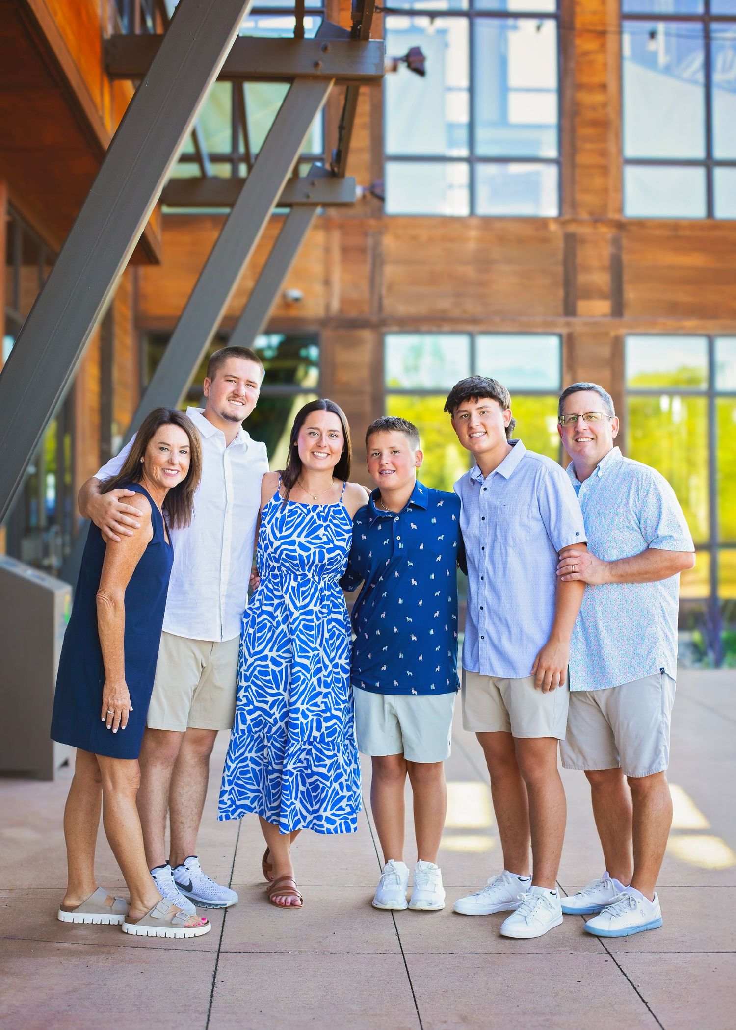 Family of six smiling together outside a modern wooden building on a sunny day.