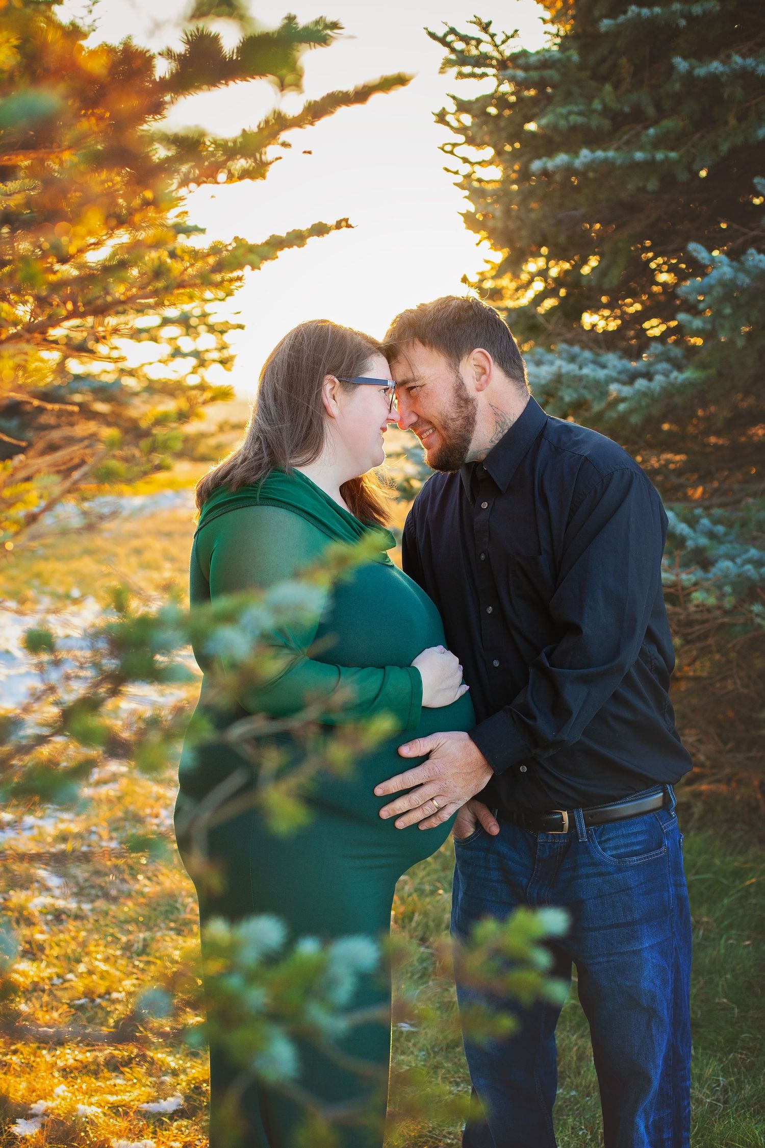 Expecting couple sharing a tender moment among pine trees during golden hour maternity shoot.
