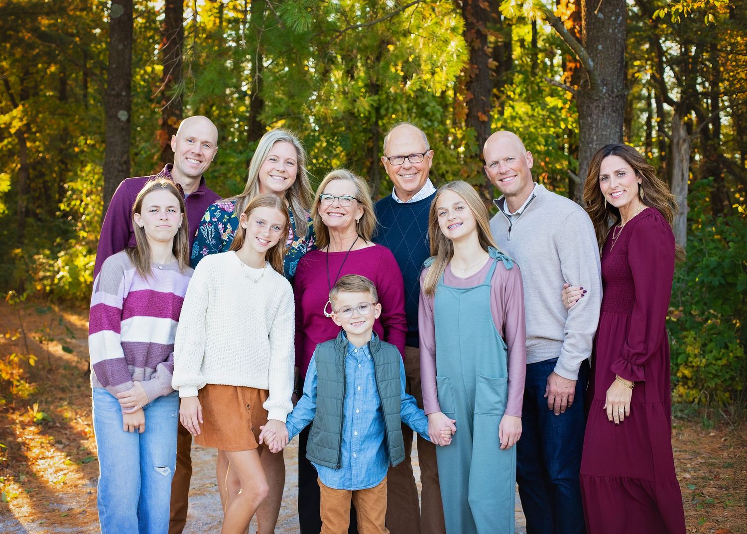 Large extended family group smiling together on a wooded path in autumn.