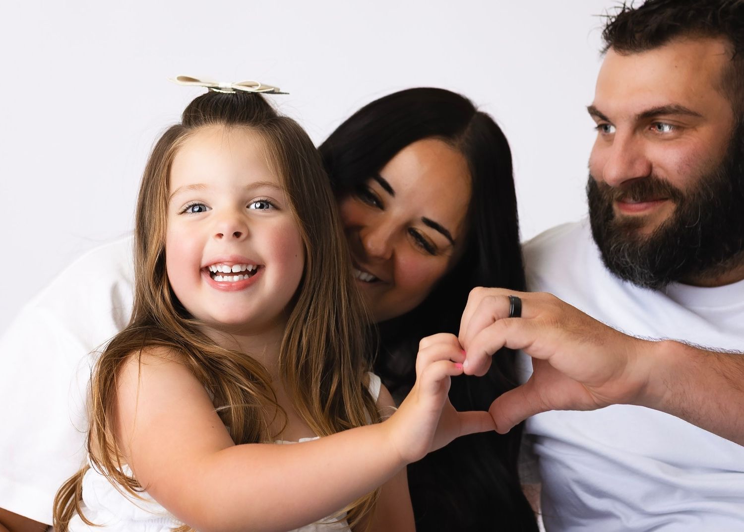 A happy family of three making a heart shape with their hands, smiling together against a white background.