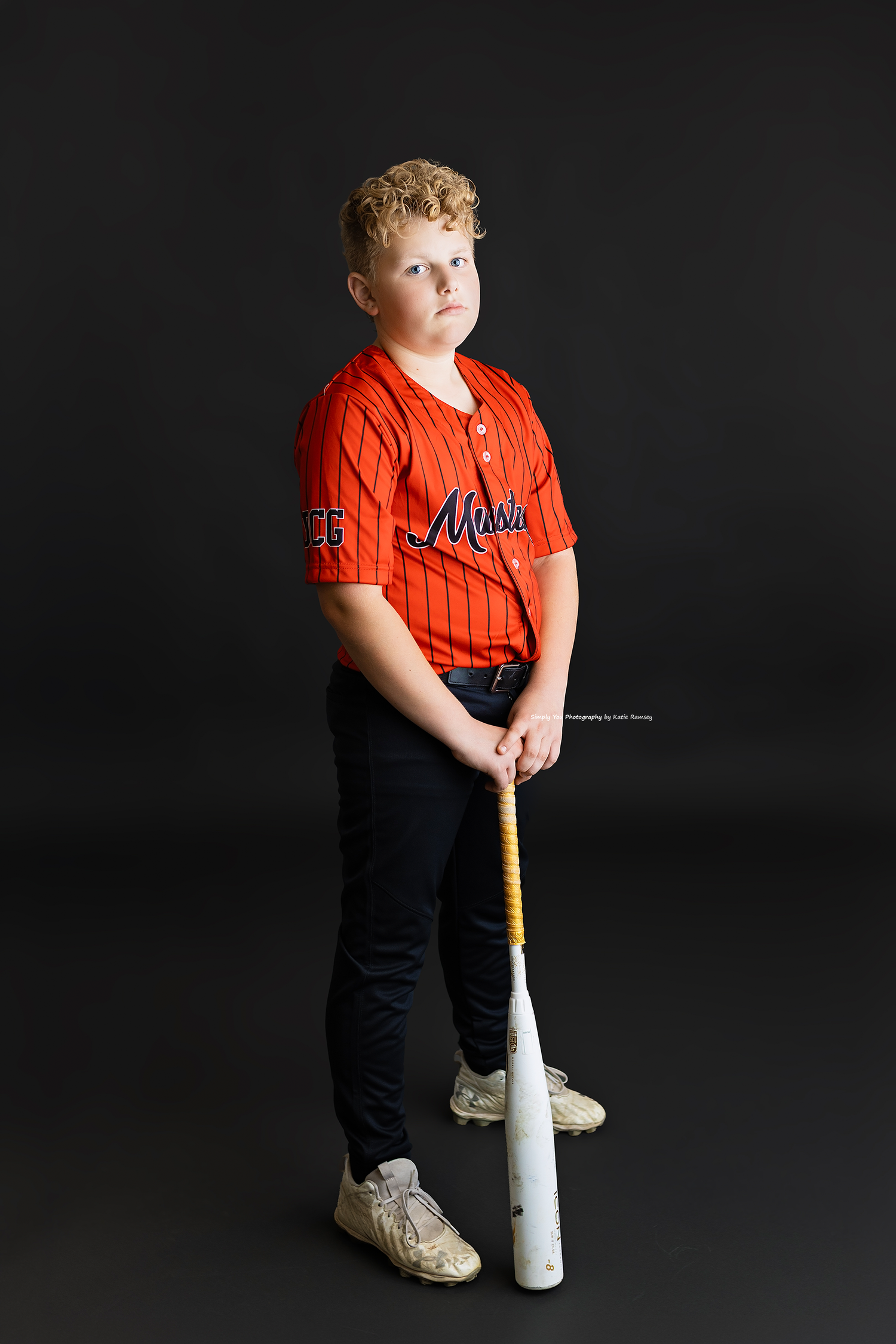 Boy in red baseball jersey holding bat, studio portrait.