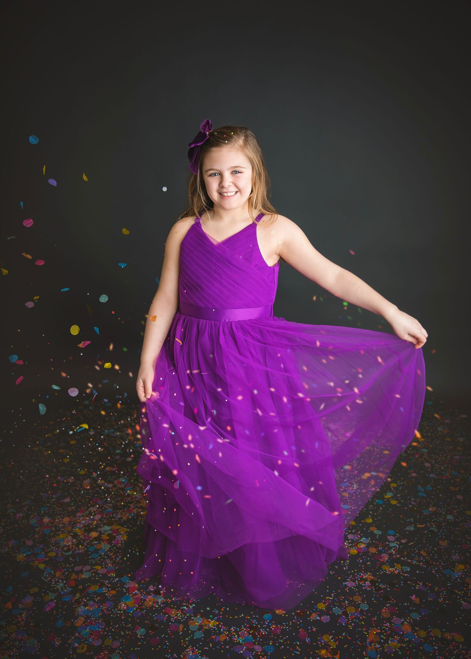 Young girl twirling in a purple dress with colorful confetti falling around her.