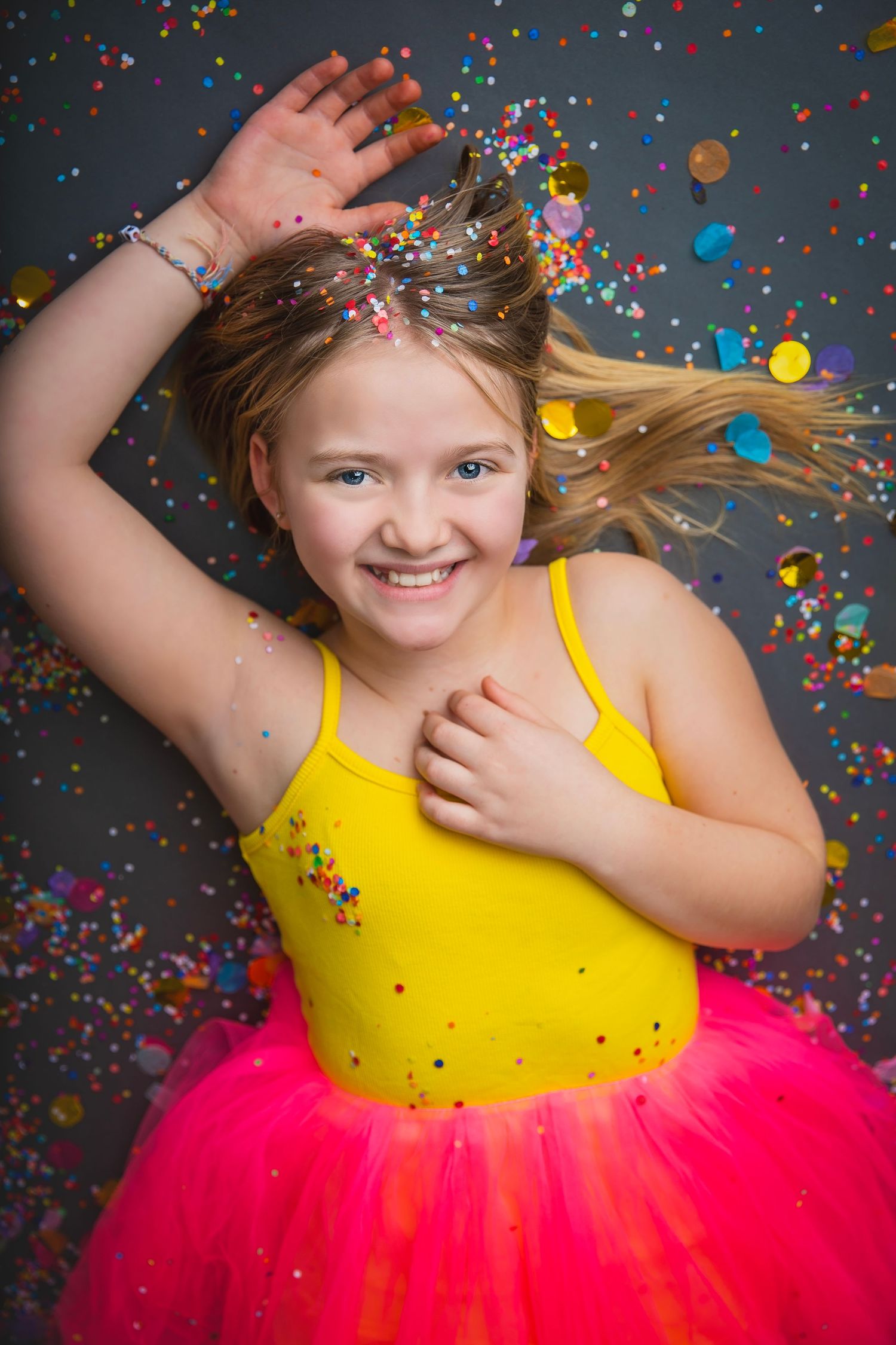 Energetic girl in yellow top and pink tutu dancing with hair flying amid falling confetti.